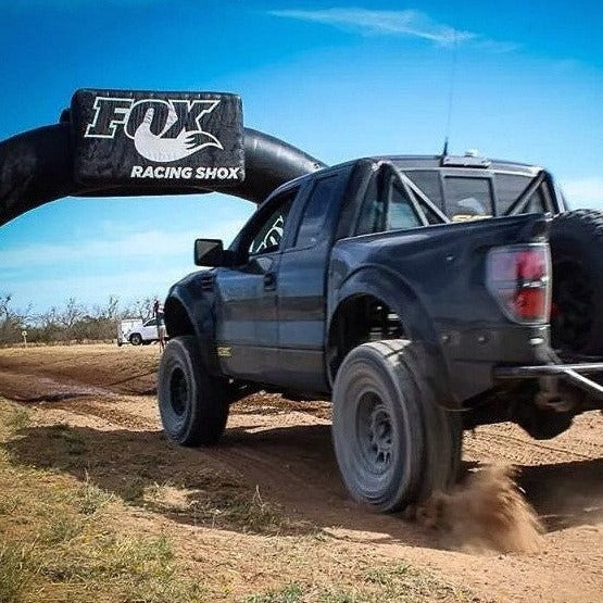 2010-2016 Ford Raptor with upgraded bedsides driving on a dirt track, showcasing offroad capabilities and performance.