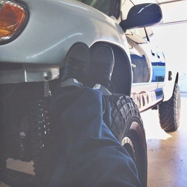 Close-up of a person's feet resting on a lifted 2000-2006 Toyota Tundra fender, showcasing offroad tires and suspension.