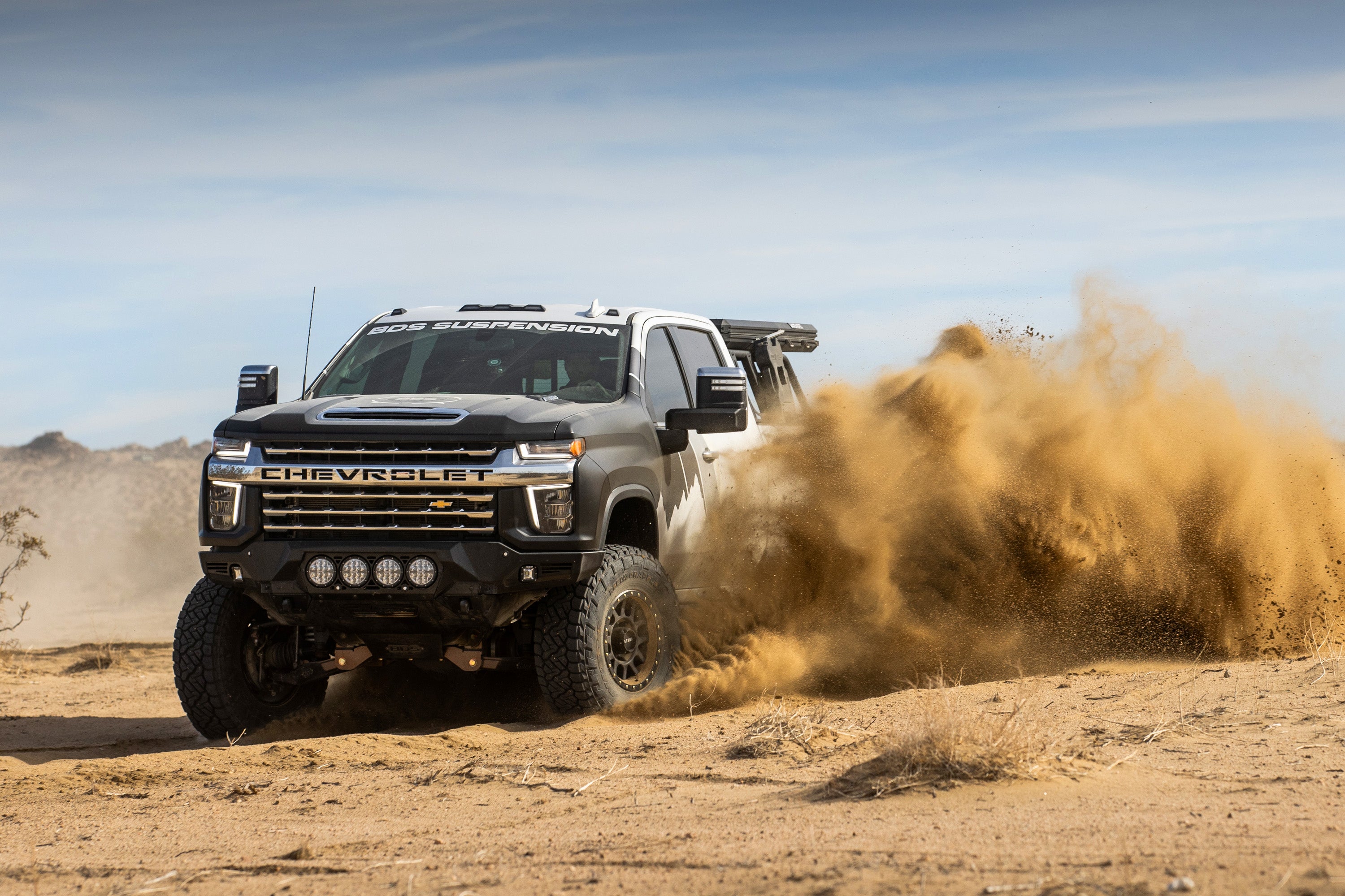 Chevy Silverado 2500HD with a 6.5-inch lift kit and FOX 2.5 coil-over conversion driving through desert sand.