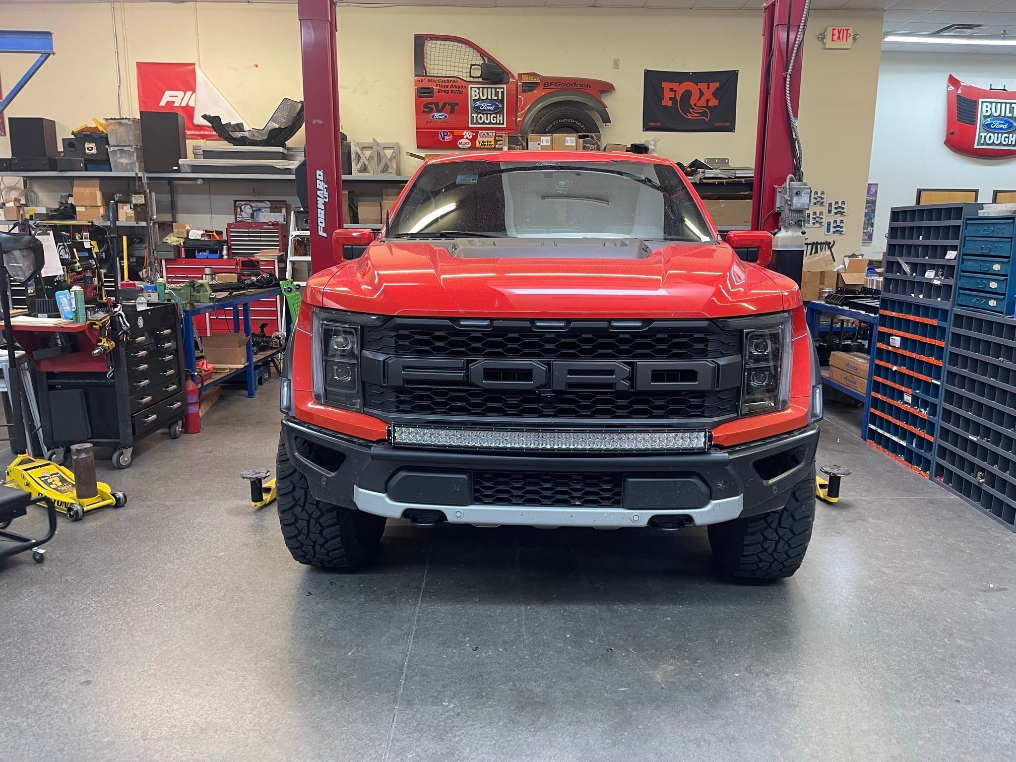 2024 Raptor Front Light Mount Kit displayed on a red Ford Raptor in a well-equipped workshop, showcasing modular bumper design.