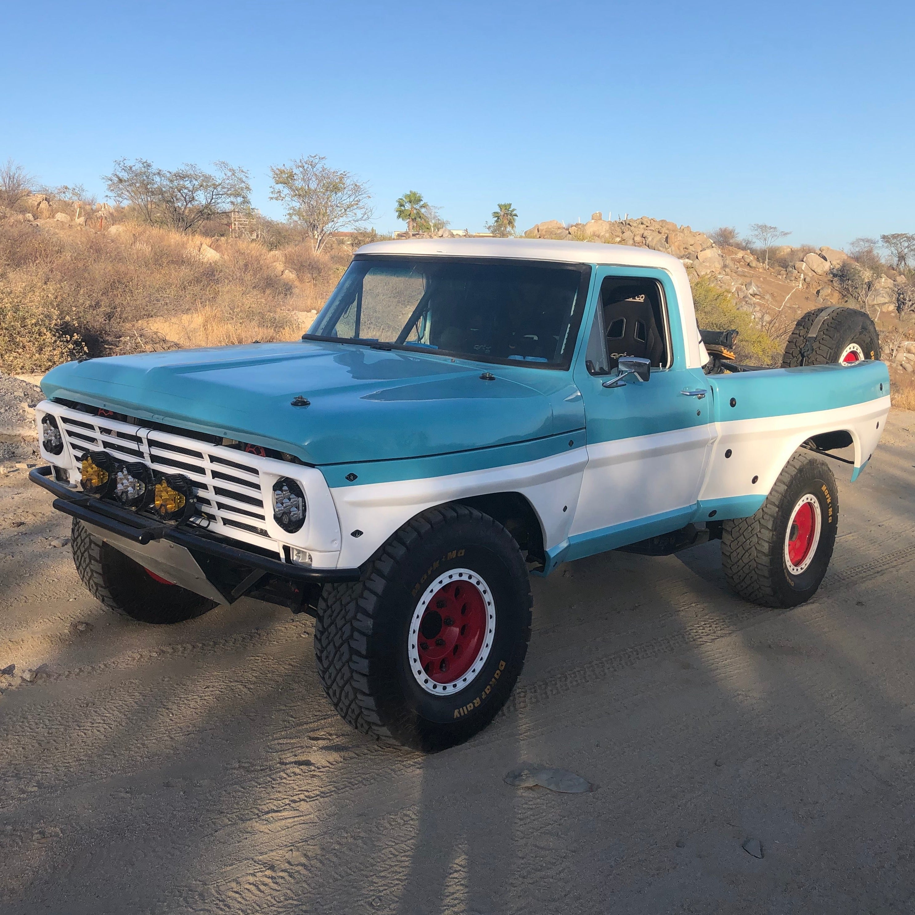 1967-1972 Ford F-100 frontend showcasing a classic truck with a two-tone blue and white paint job and off-road tires.