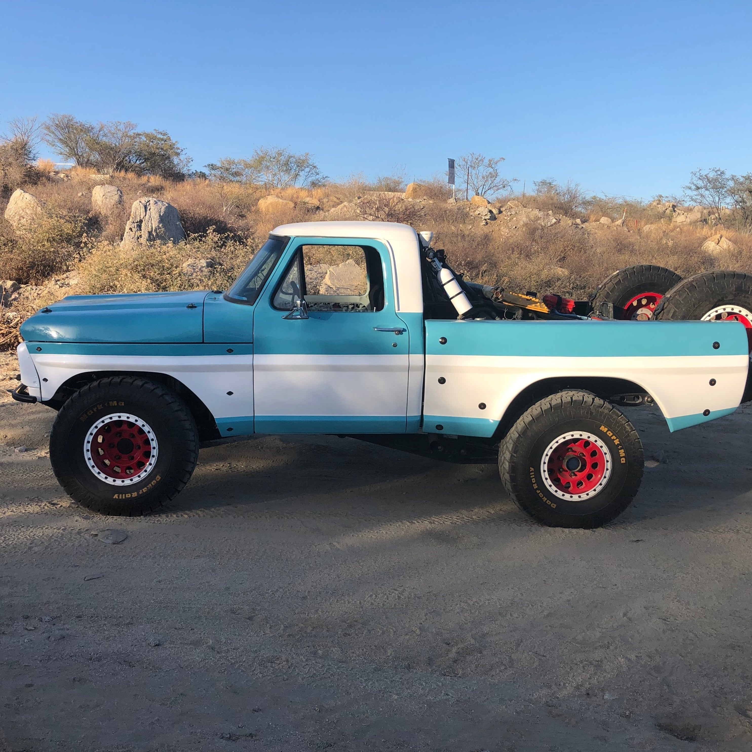 1967-1972 Ford F-100 with a custom frontend, showcasing a blue and white paint job, offroad tires, and rugged terrain.
