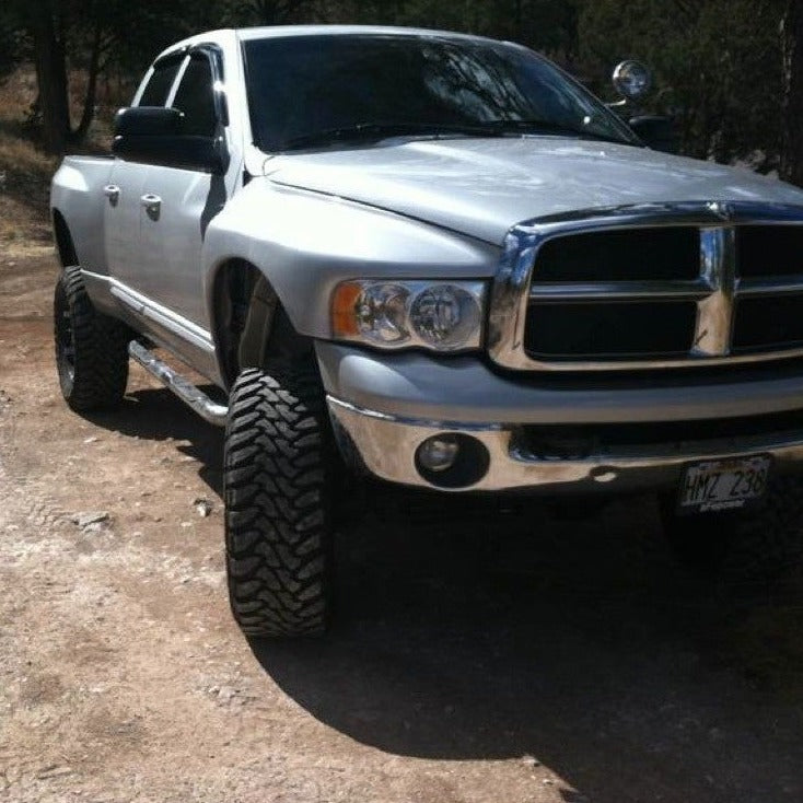 2003-2005 Dodge Ram with aftermarket fenders and offroad tires, showcasing a lifted stance in a natural setting.