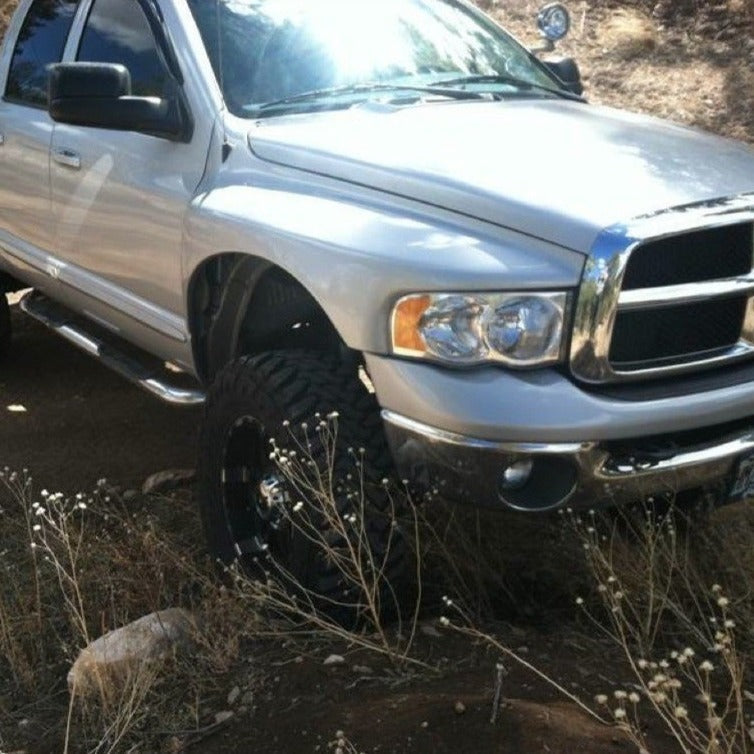 2003-2005 Dodge Ram fenders installed on a lifted silver truck, showcasing offroad tires and rugged terrain.