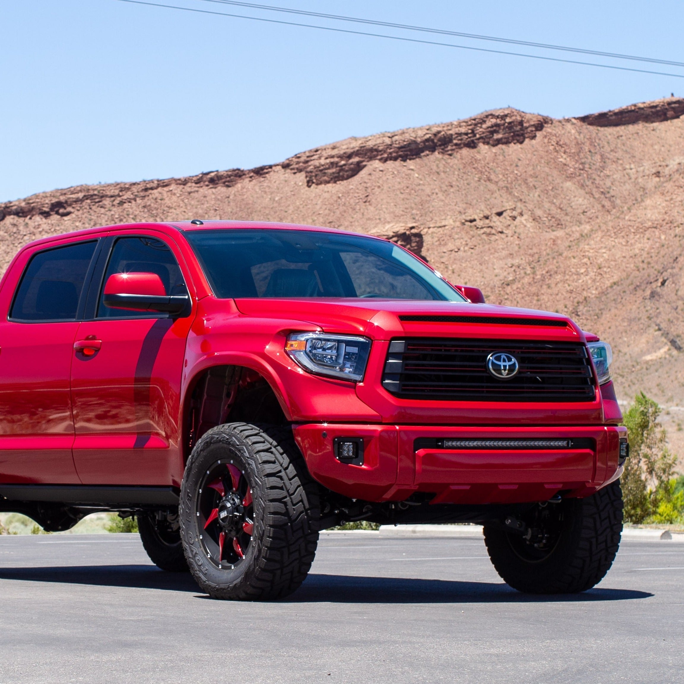 2014-2021 Toyota Tundra with custom fenders, showcasing a bold red exterior and off-road tires in a desert setting.