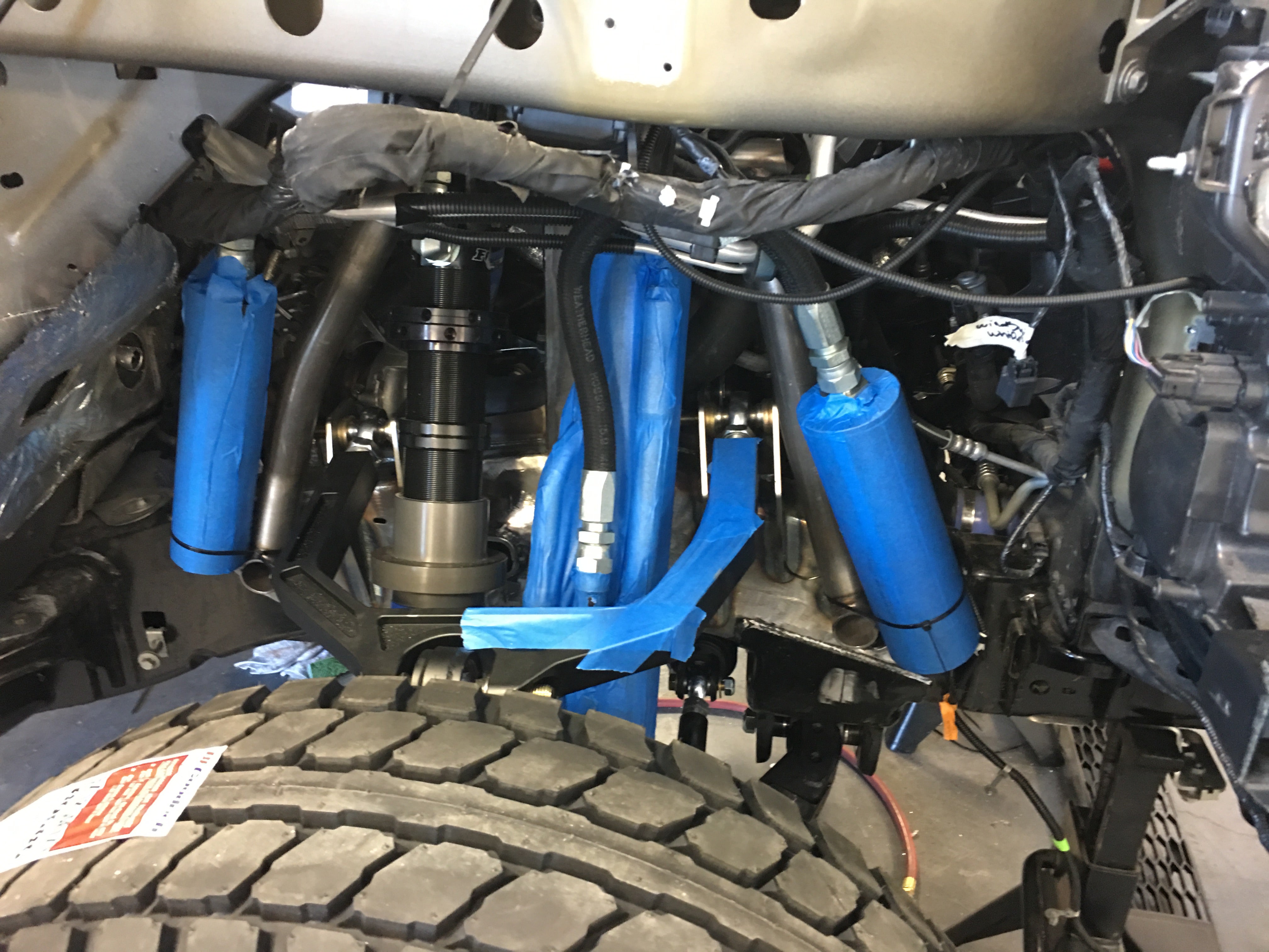 2017 Up Raptor Long Travel Front Suspension Kit installed, showcasing components and blue protective covers in a truck chassis.
