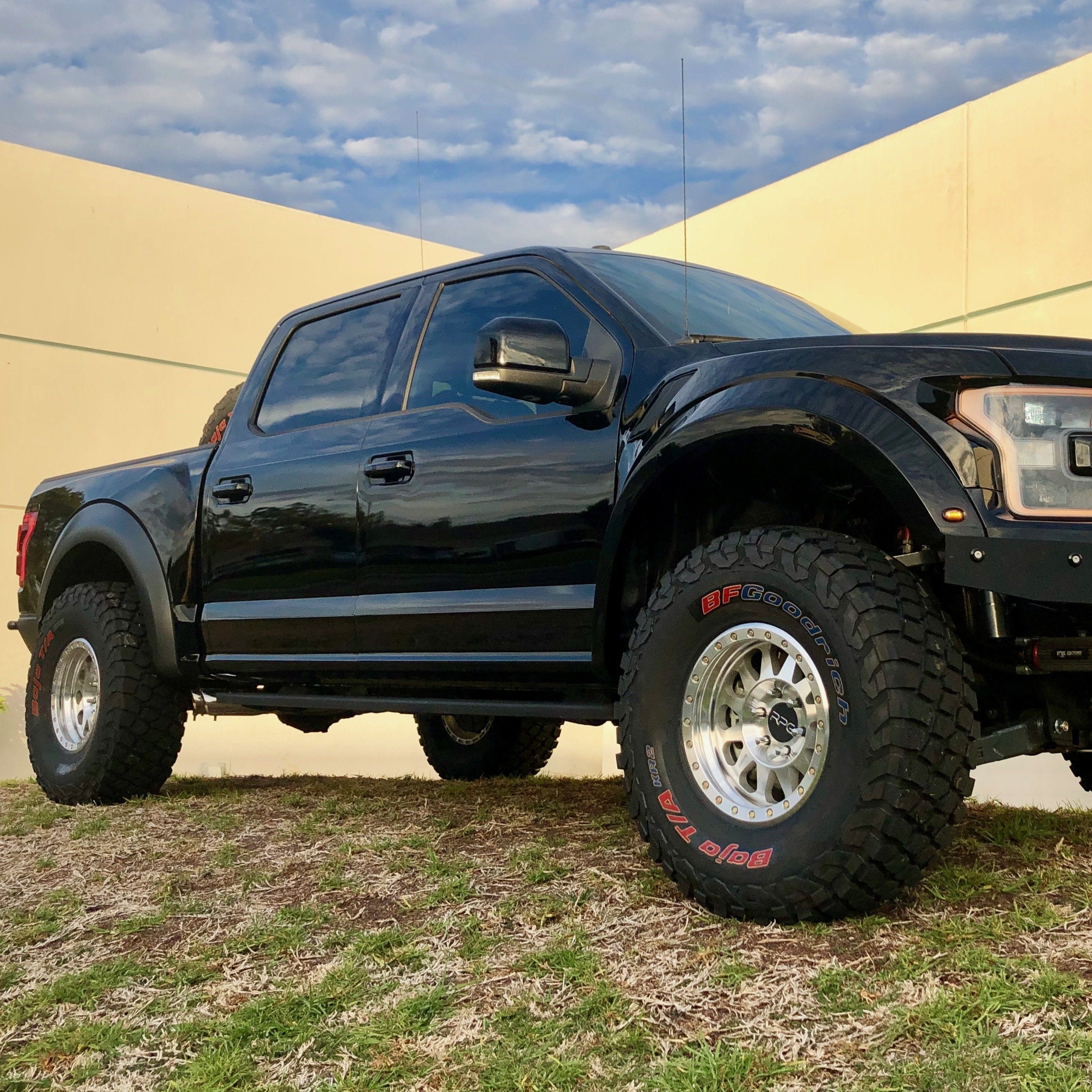 2017-2020 Ford Raptor fenders showcasing a black truck with offroad tires and elevated stance on grassy terrain.