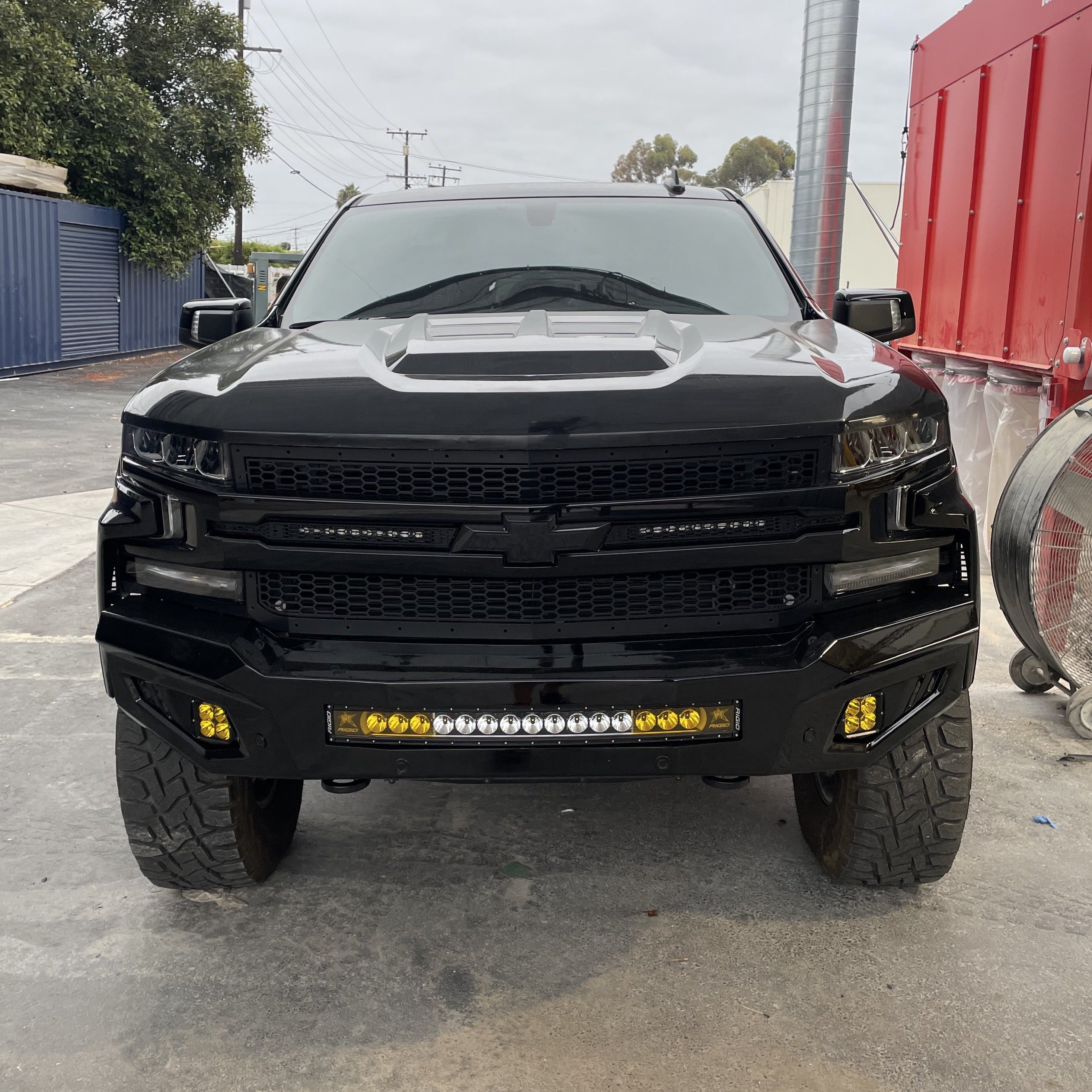Front view of a black 2019-2025 Chevrolet Silverado with a custom hood and off-road lights, showcasing its rugged design.