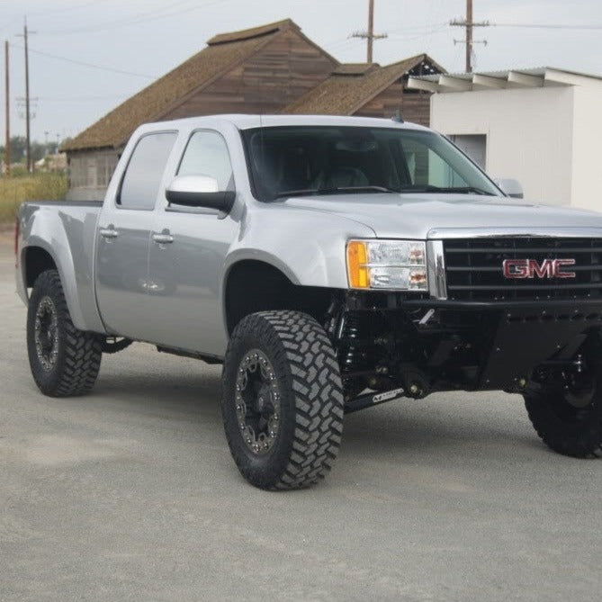 Silver 2007-2013 GMC Sierra with upgraded fenders and off-road tires parked on gravel, showcasing its rugged design.