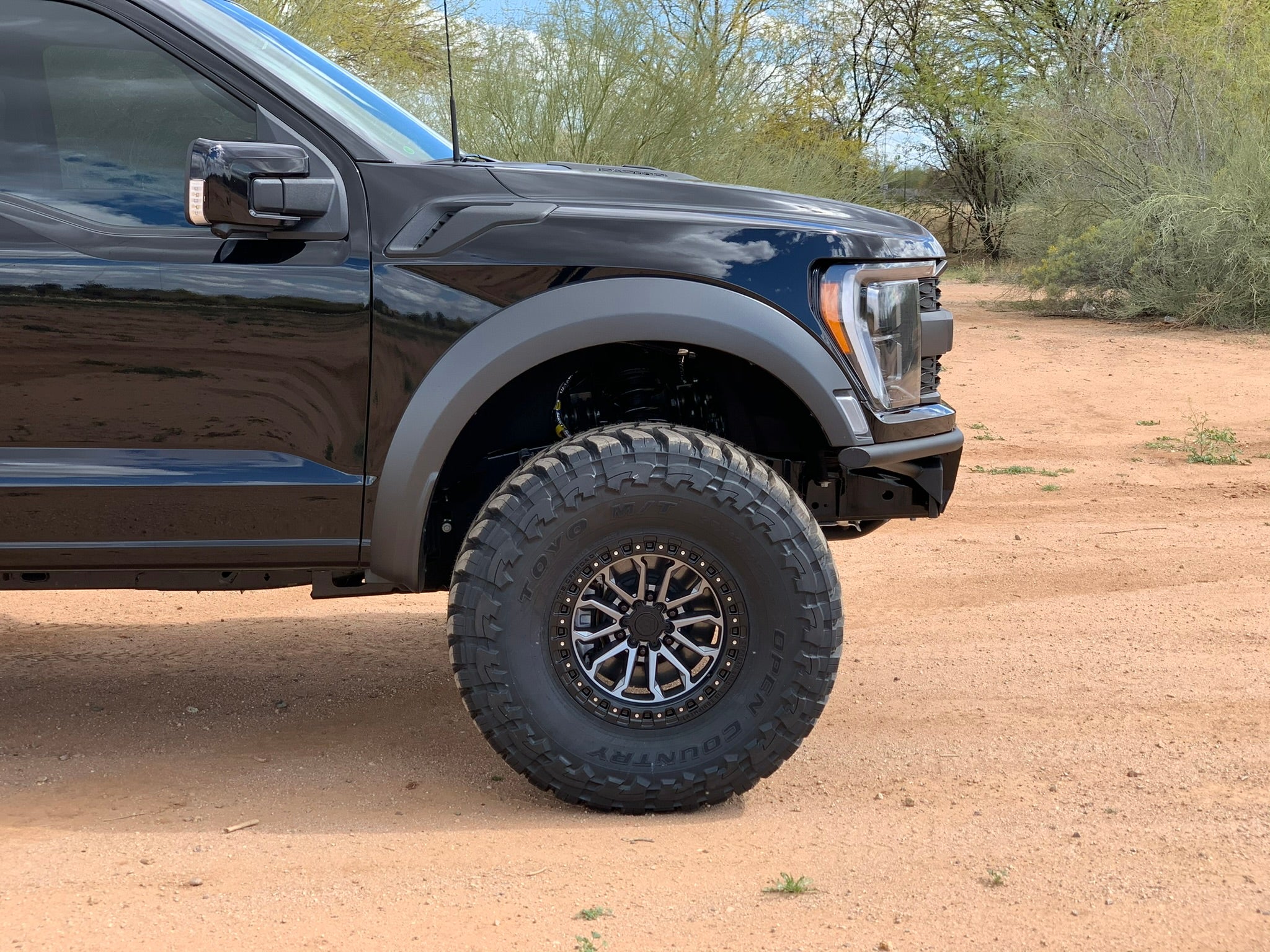 2021 and up Raptor front leveling kit showcasing a 2-inch lift with rugged tires on a black truck in a desert setting.