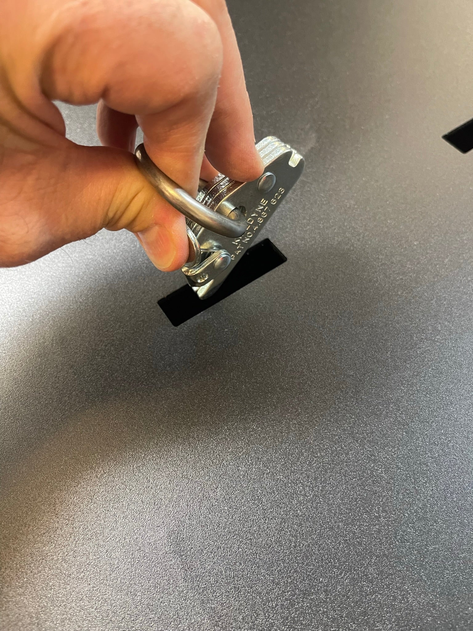 Hand holding a locking mechanism over a slot on a textured surface of a 2017-2024 Raptor rear bed organizer.