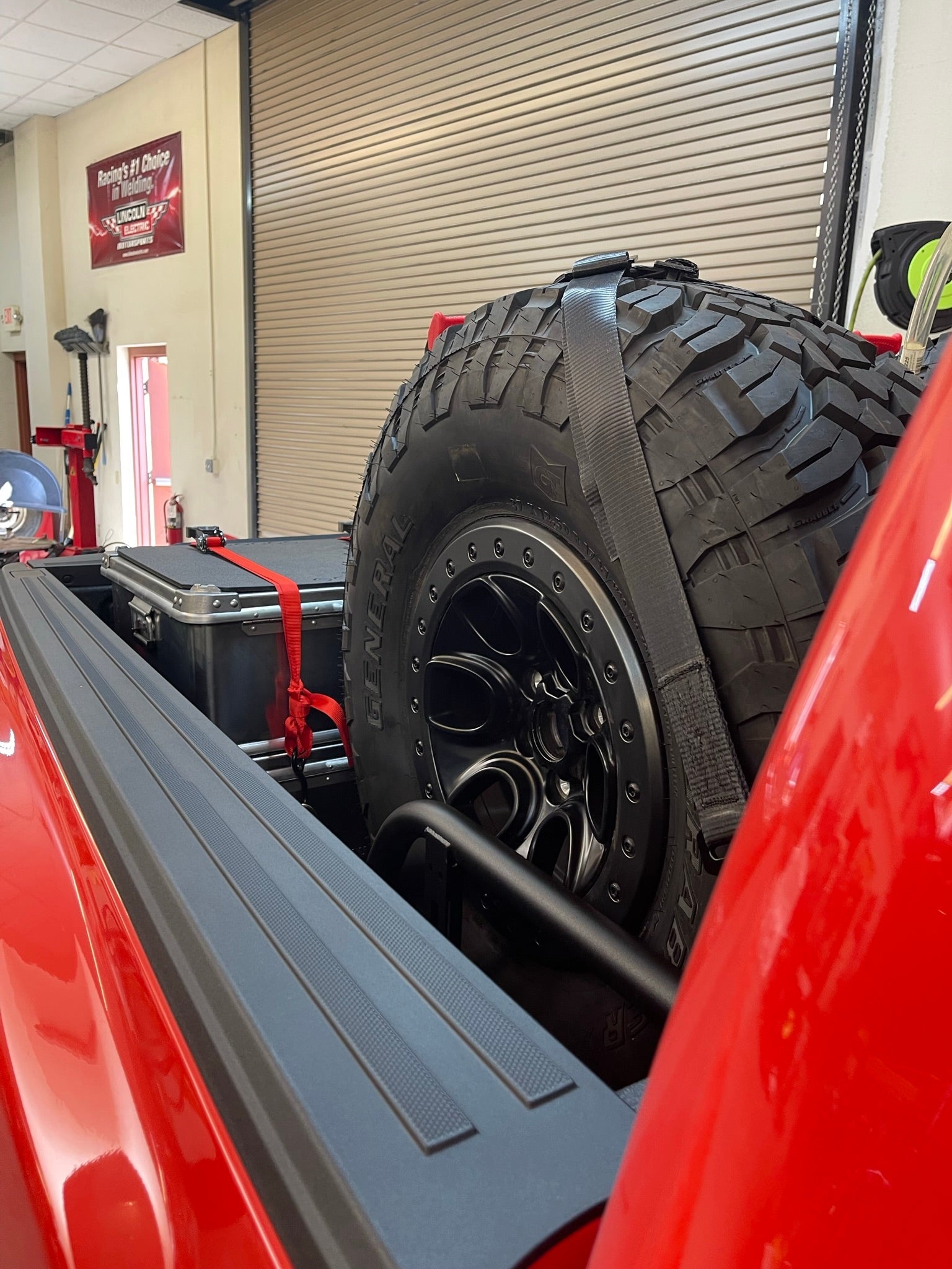 Raptor rear bed organizer with cargo slide tray, featuring a mounted spare tire and storage container in a truck bed.