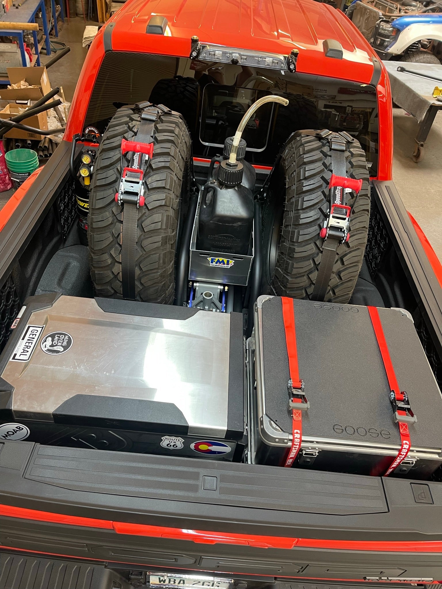 Rear view of a 2017-2024 Raptor truck bed featuring a cargo slide tray with organized gear, including tires and storage cases.