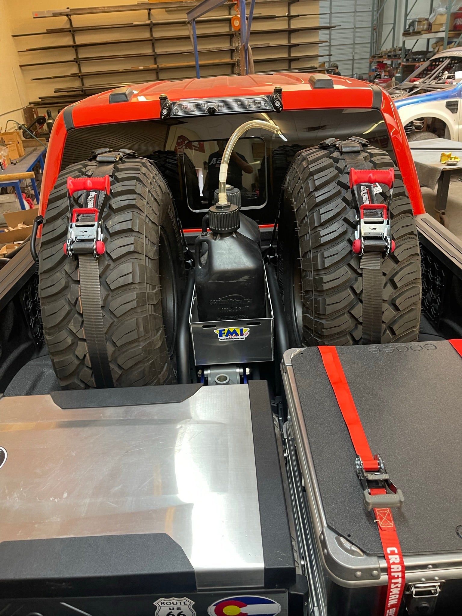 Raptor rear bed organizer with cargo slide tray, featuring secured spare tires and storage containers in a truck bed.