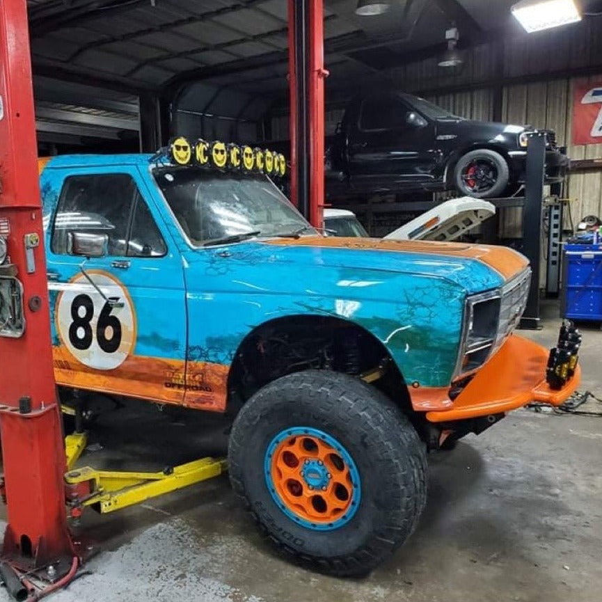 1980-1986 Ford Bronco with custom fenders, showcasing vibrant paint and off-road tires in a garage setting.