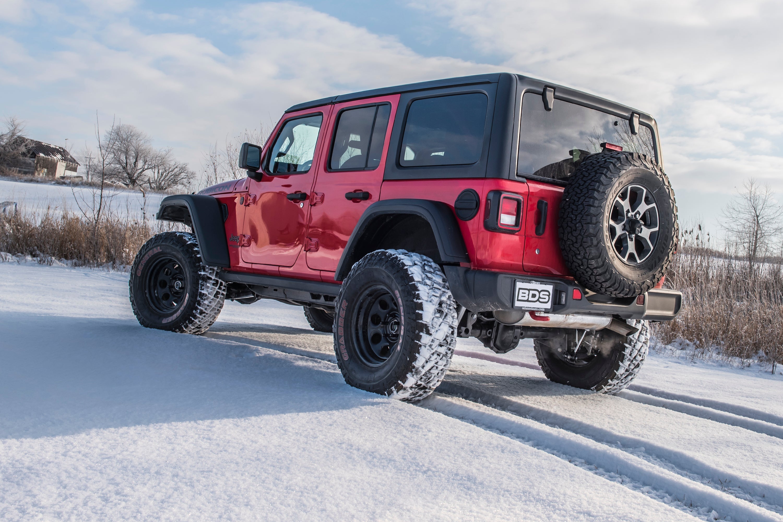 Red Jeep Wrangler JL with a 2-inch lift kit parked on snow-covered ground, showcasing its off-road capabilities and rugged design.
