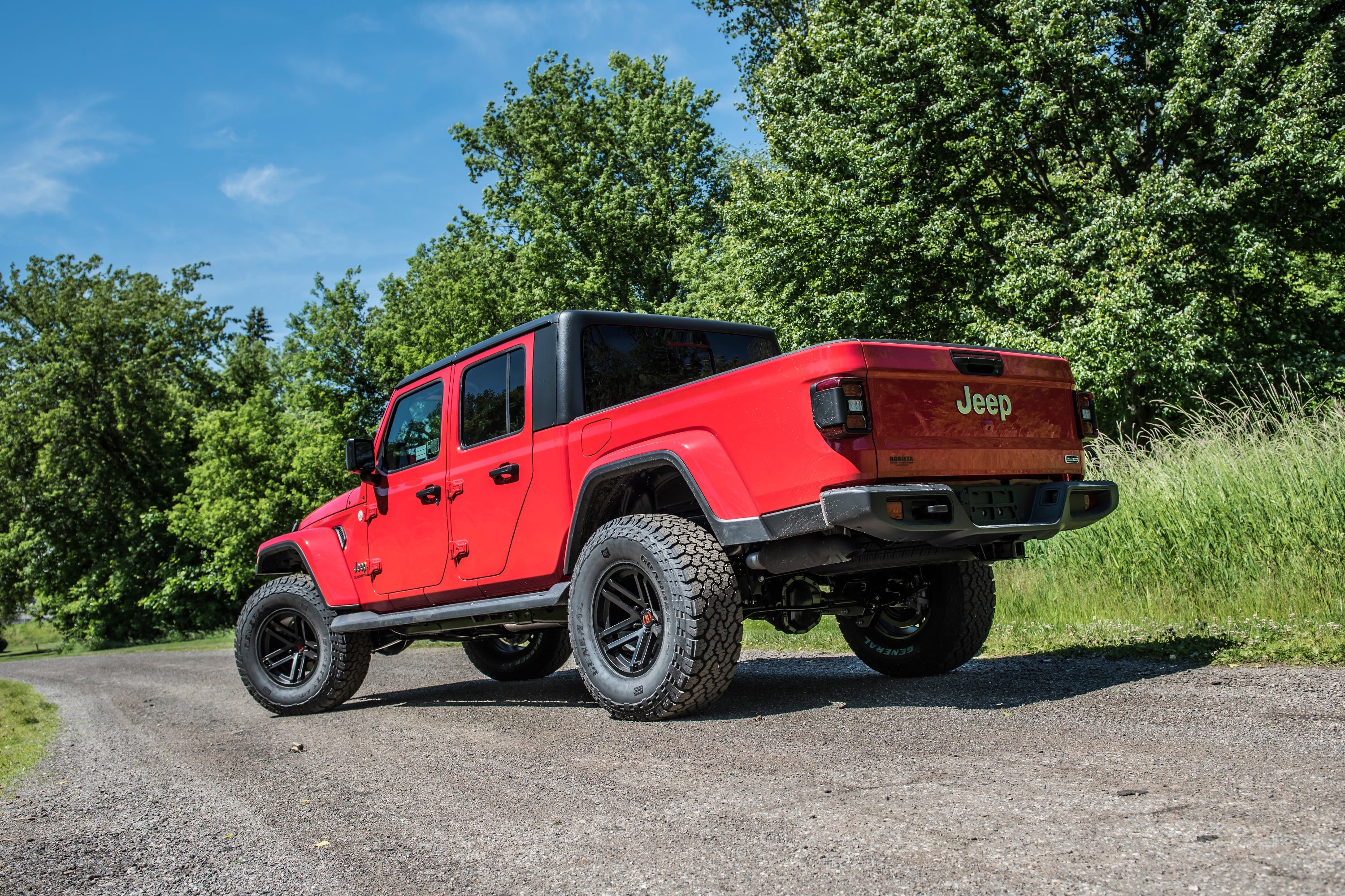 Red Jeep Gladiator JT with a 2-inch lift kit parked on a gravel road surrounded by greenery, showcasing its off-road capabilities.