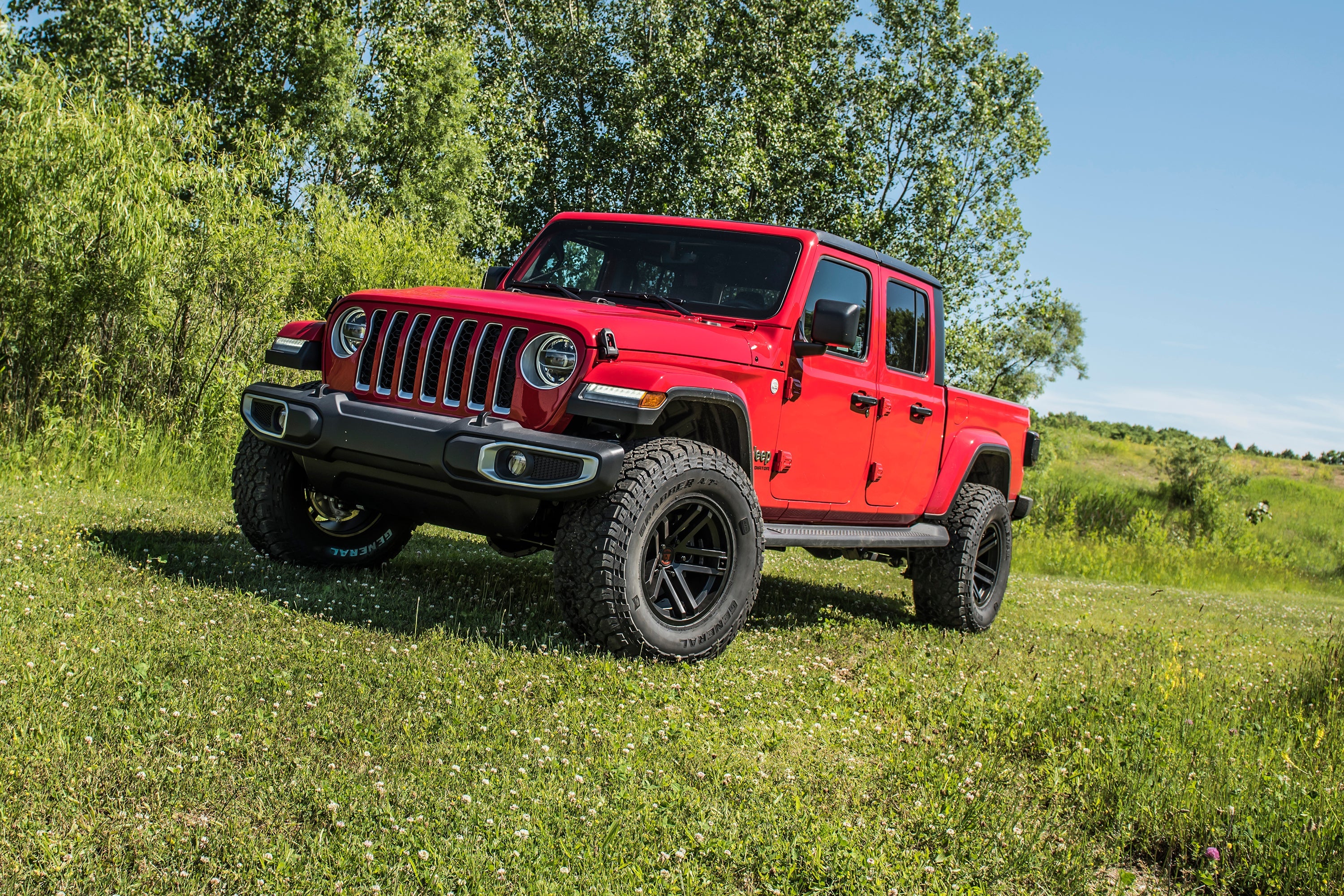 Red Jeep Gladiator JT with a 2-inch leveling kit parked on grass, showcasing enhanced off-road stance and rugged tires.
