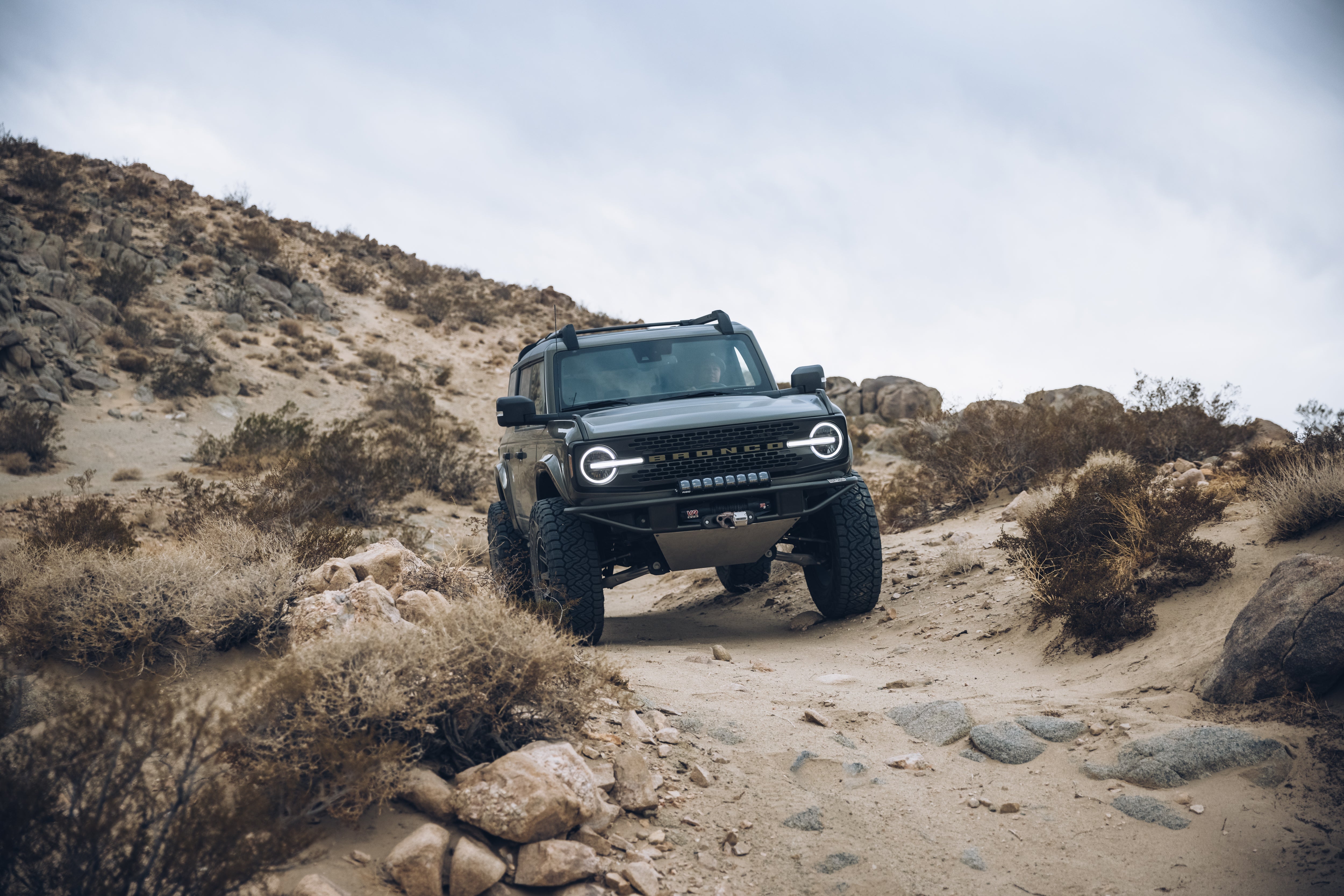 2021 Ford Bronco Outer Banks with BAJA FORGED parts navigating a rugged off-road terrain in a desert landscape.