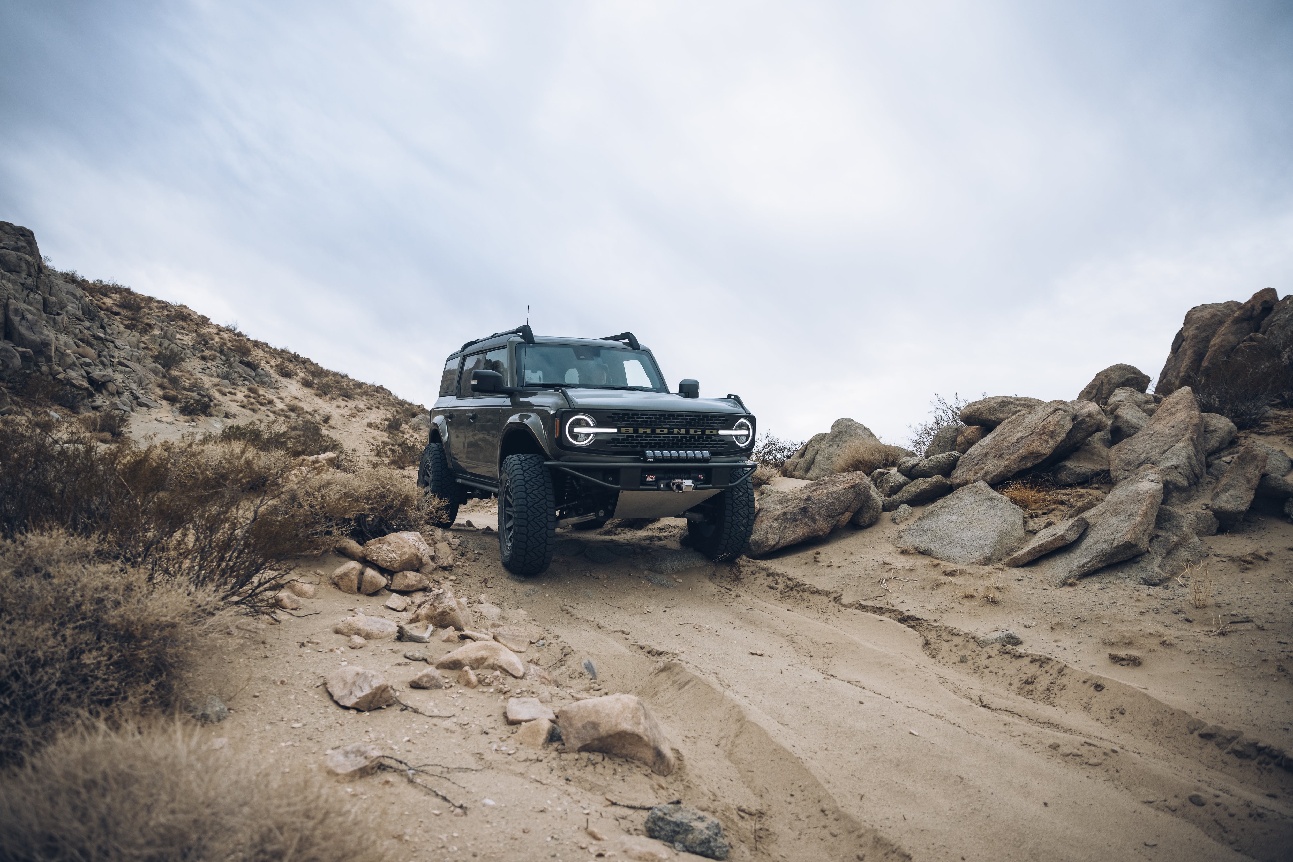 2021 Outer Banks Bronco with BAJA FORGED parts navigating rocky terrain in a desert landscape.