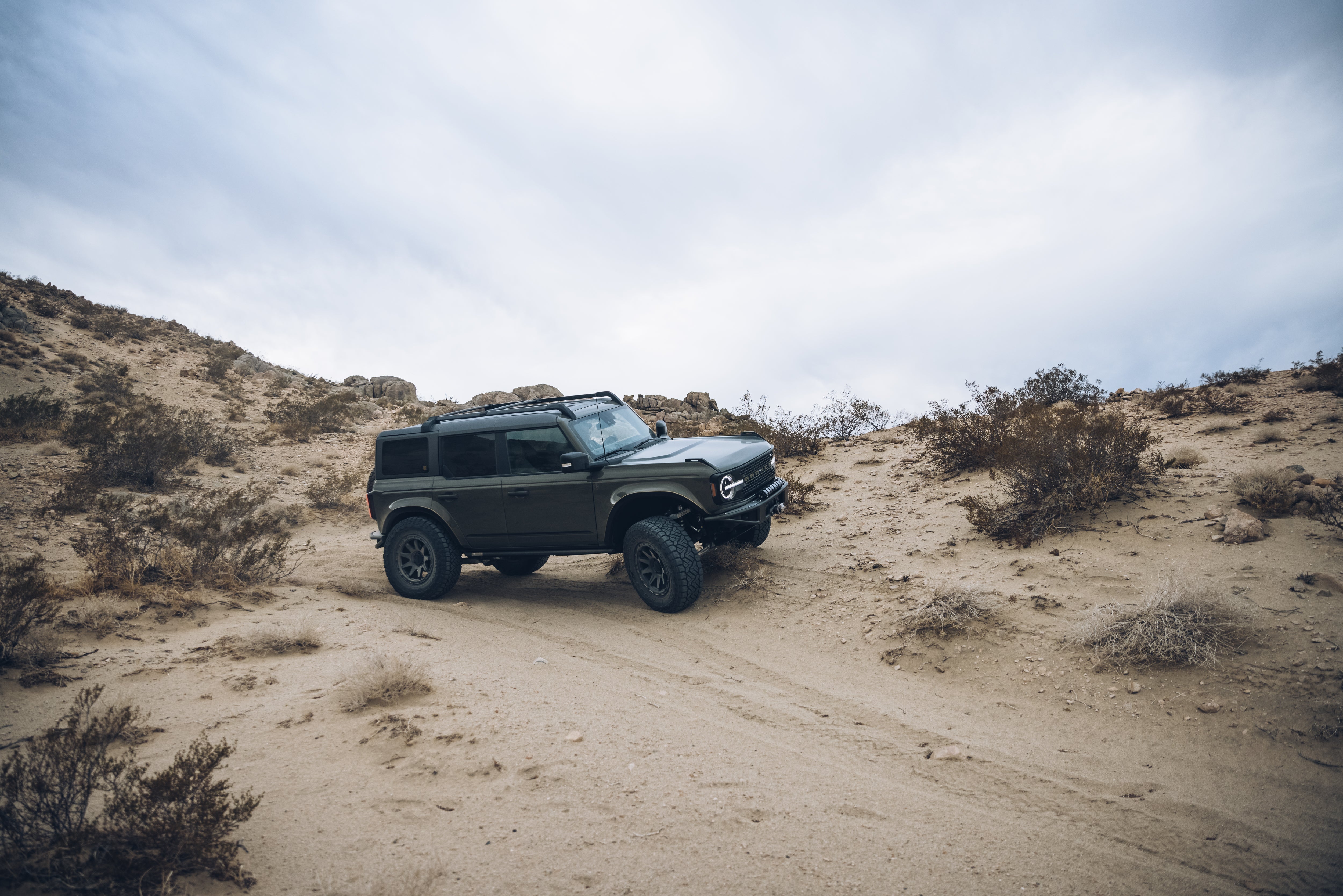 2021 Outer Banks vehicle from BAJA FORGED navigating a rugged desert terrain with rocky hills and sparse vegetation.