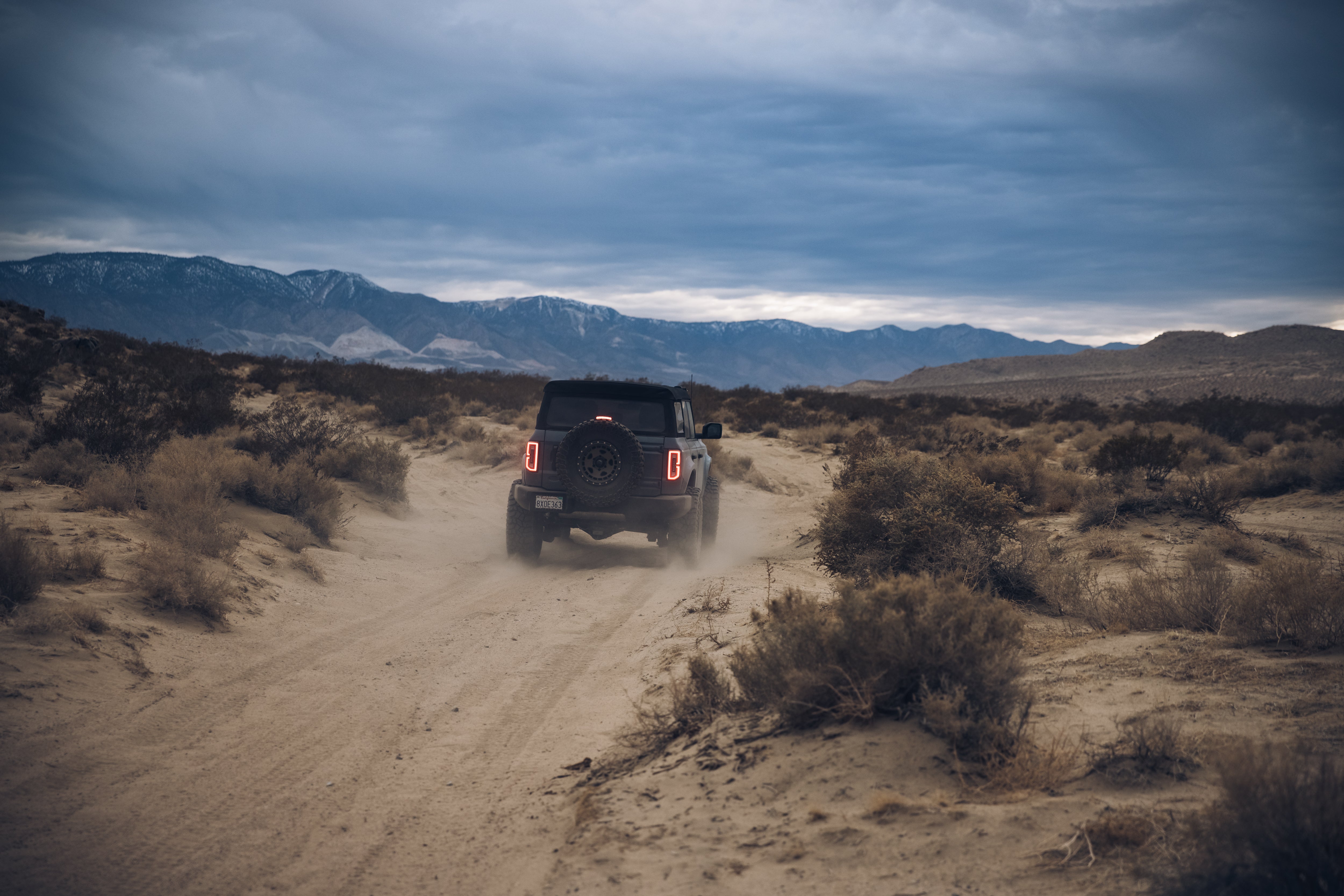 ADV Fiberglass 2021 Ford driving on a dusty off-road trail with mountains in the background, showcasing rugged terrain.