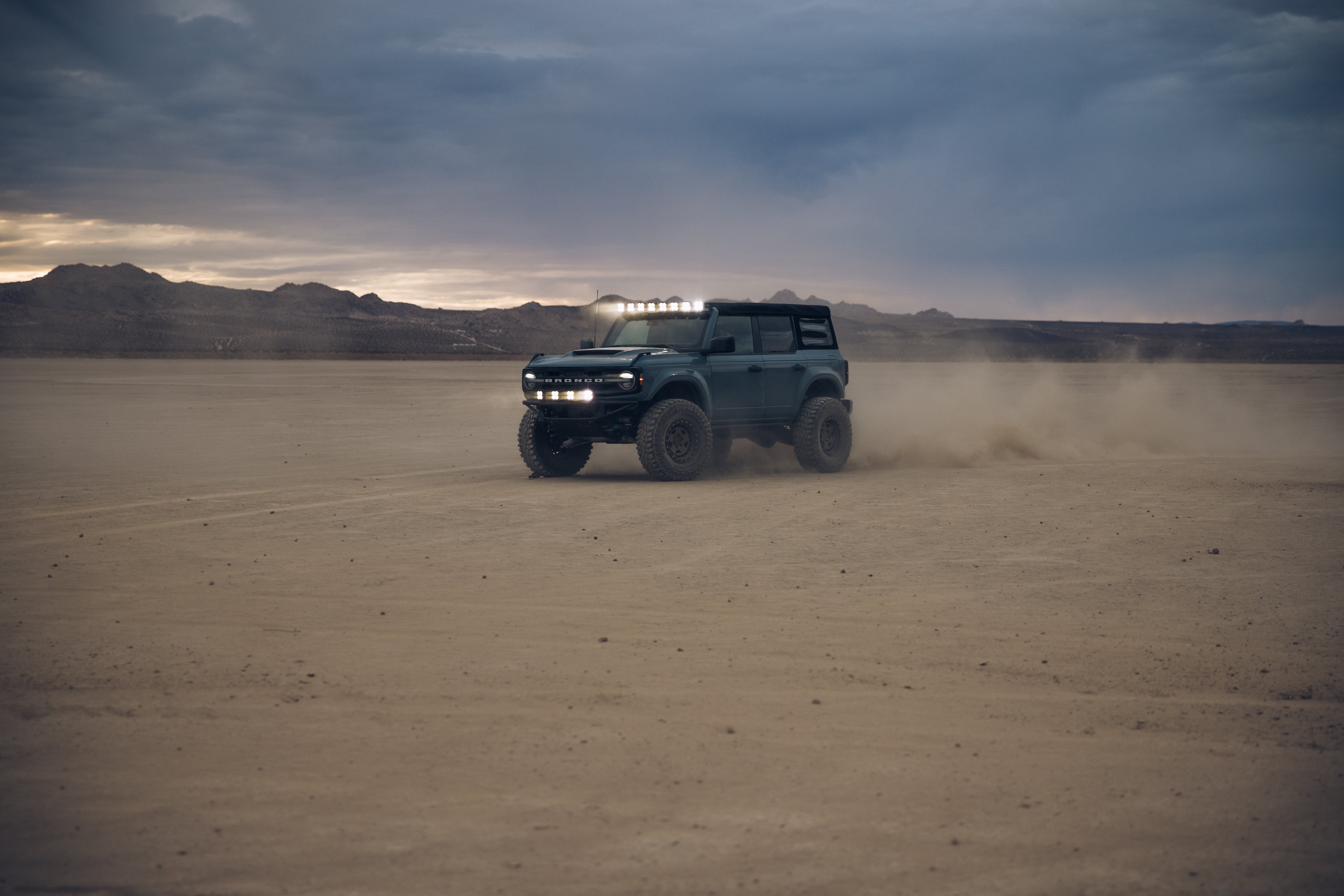 ADV Fiberglass 2021 Ford off-road vehicle driving through a dusty desert landscape with dramatic lighting.
