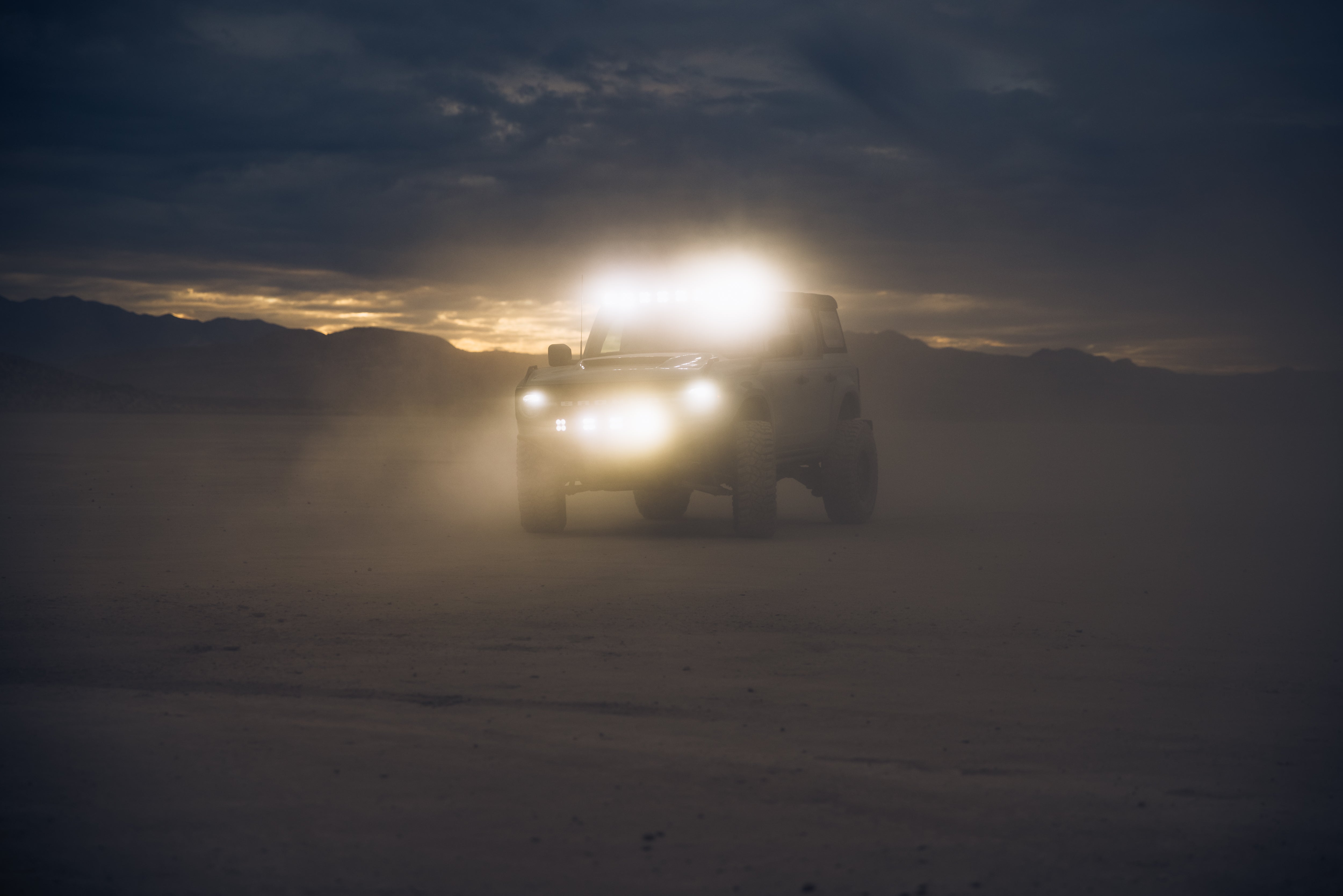 ADV Fiberglass 2021 Ford off-road vehicle with bright lights driving through dusty terrain at sunset.