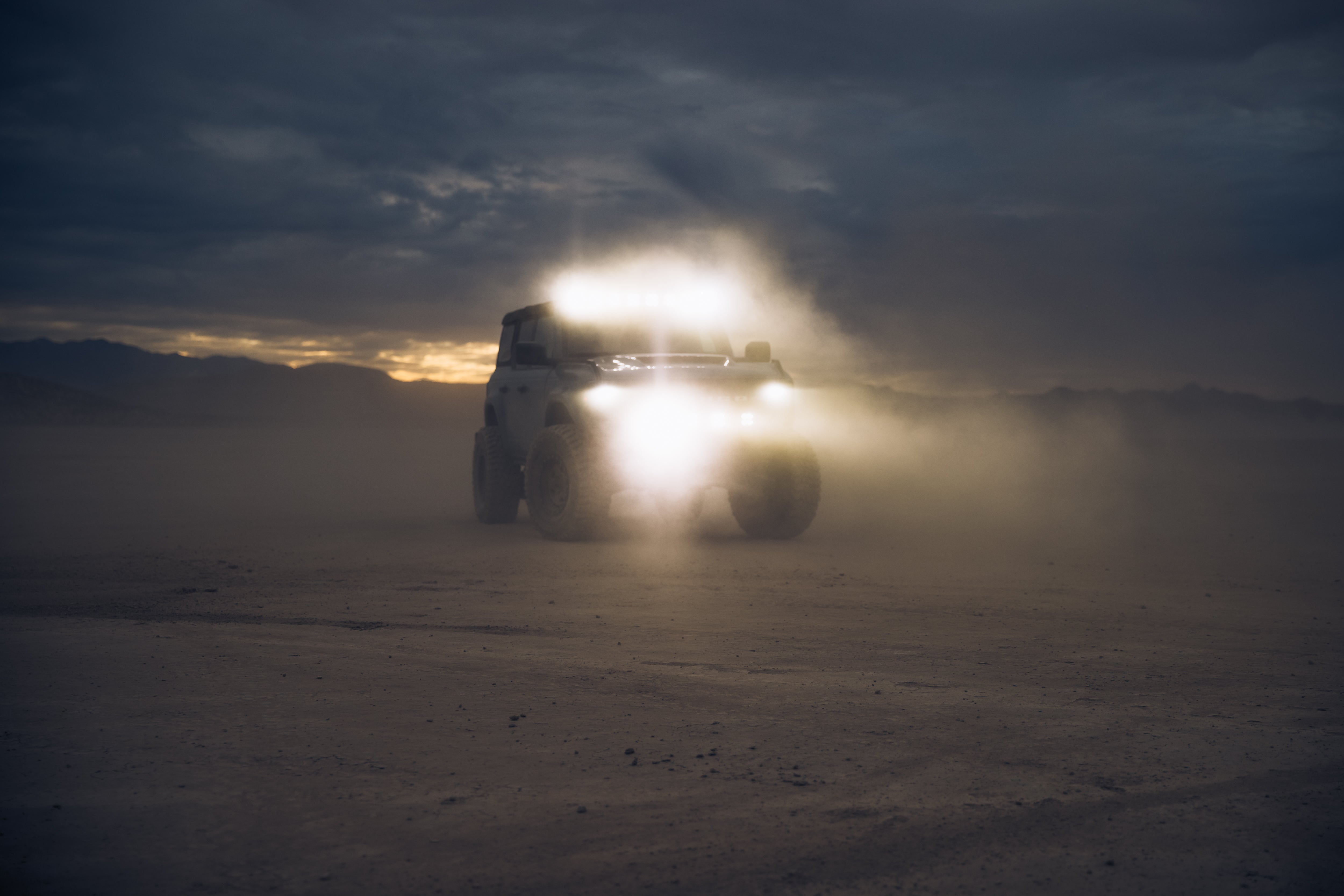 ADV Fiberglass 2021 Ford off-road vehicle with bright lights driving through dusty terrain at sunset.