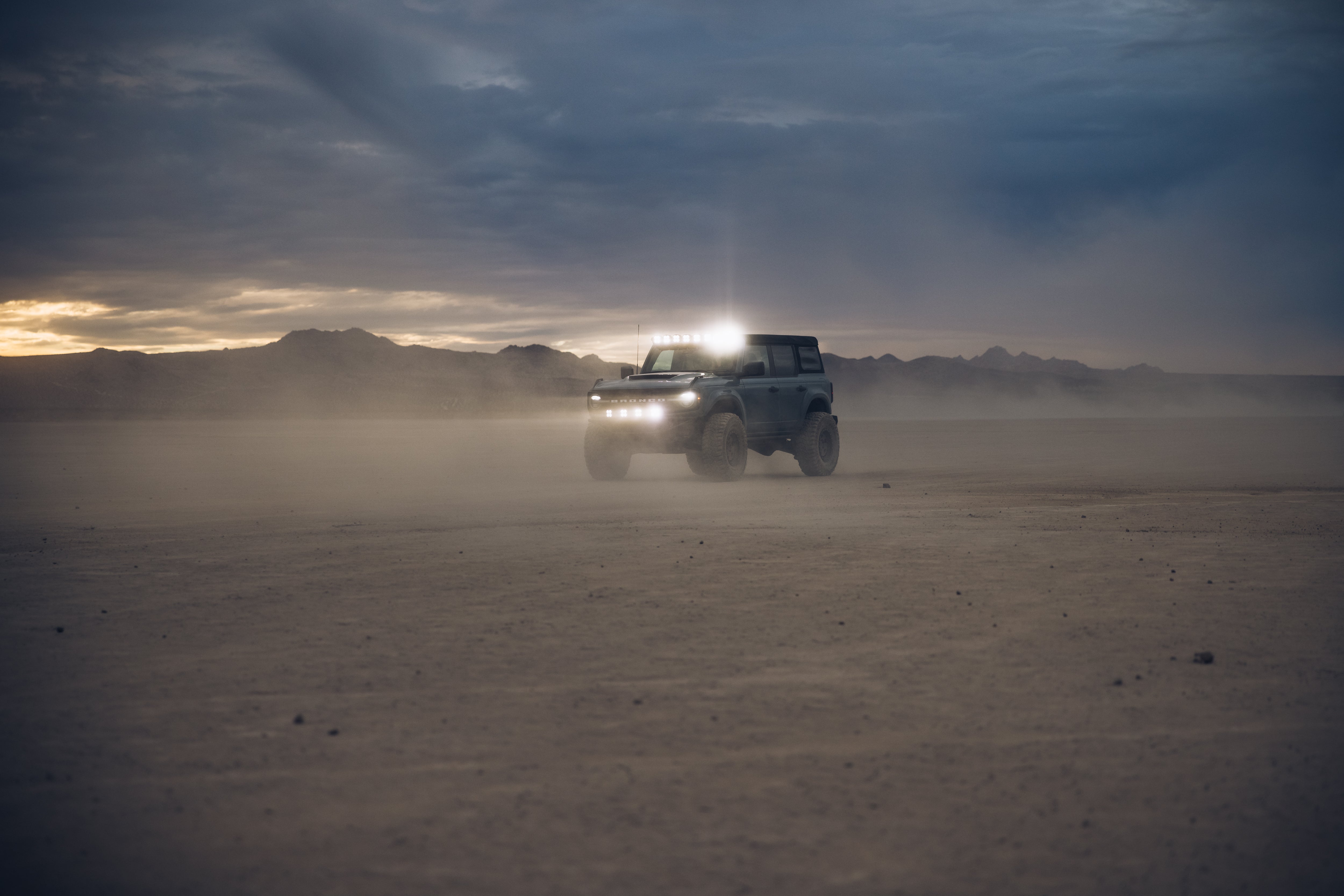 ADV Fiberglass 2021 Ford driving through a dusty desert landscape with off-road lights illuminated at dusk.