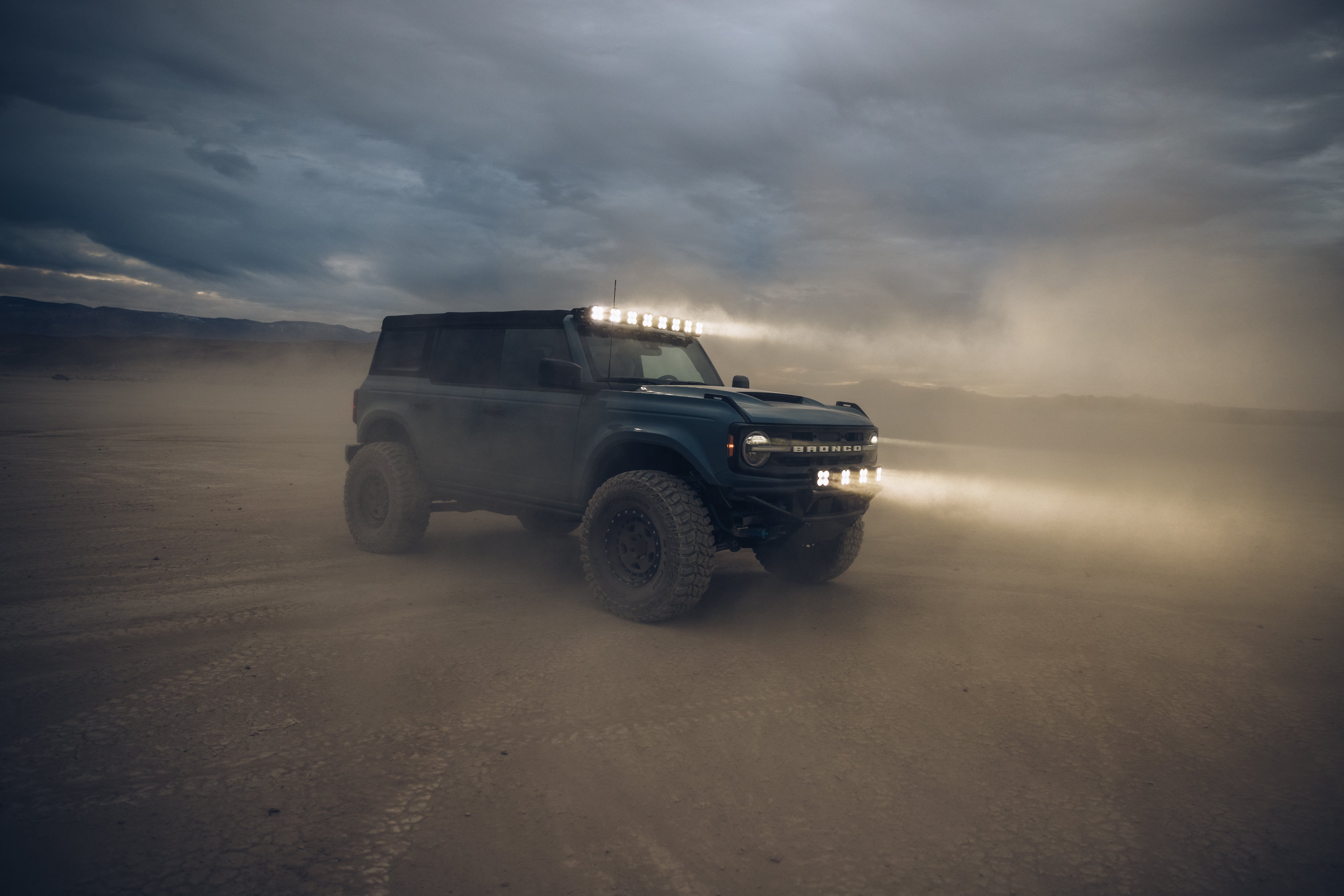 ADV Fiberglass 2021 Ford Bronco with off-road lights in a dusty landscape, showcasing rugged design and performance.