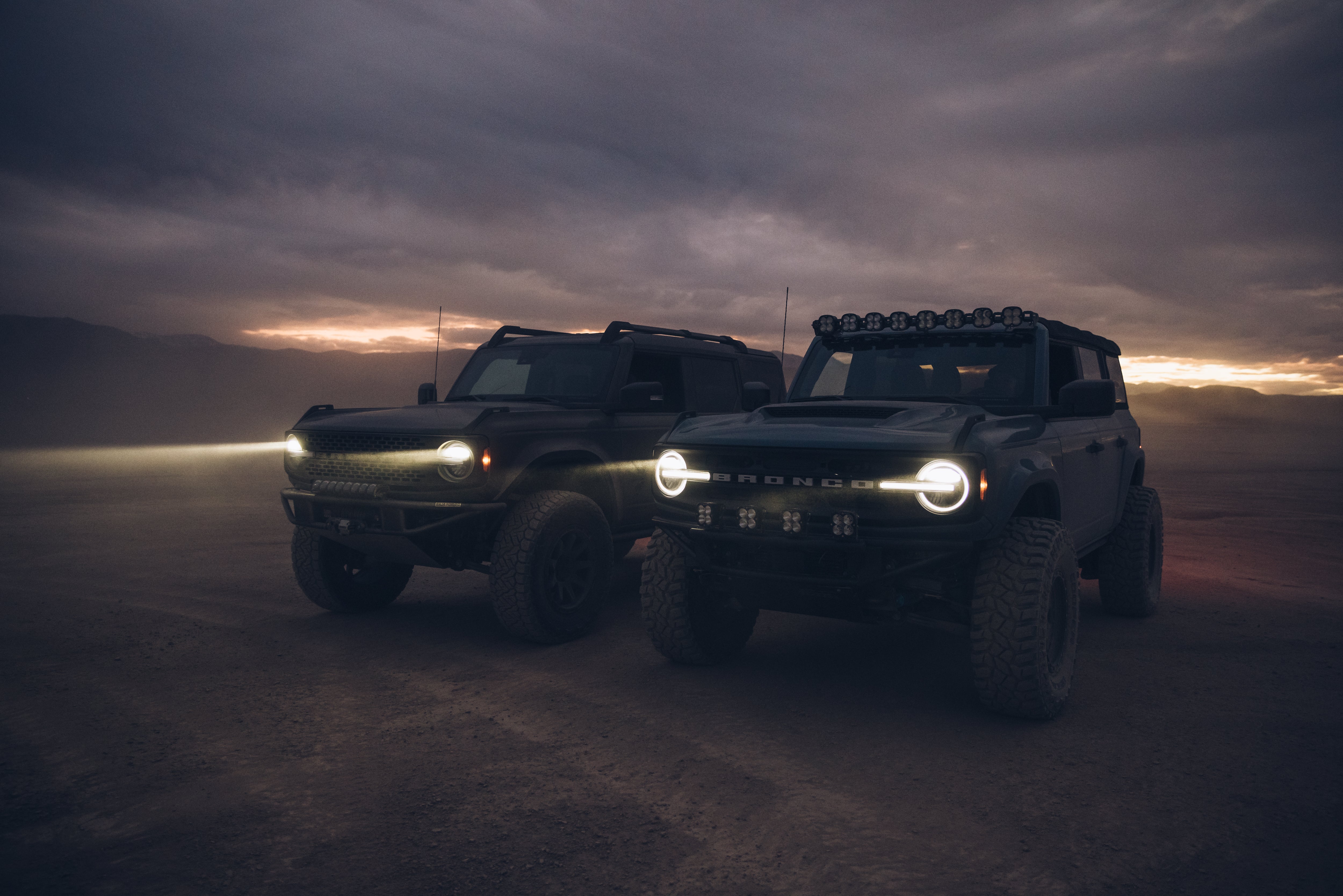 Two modified 2021 Ford Bronco vehicles in a rugged outdoor setting, showcasing ADV fiberglass parts and off-road capabilities.