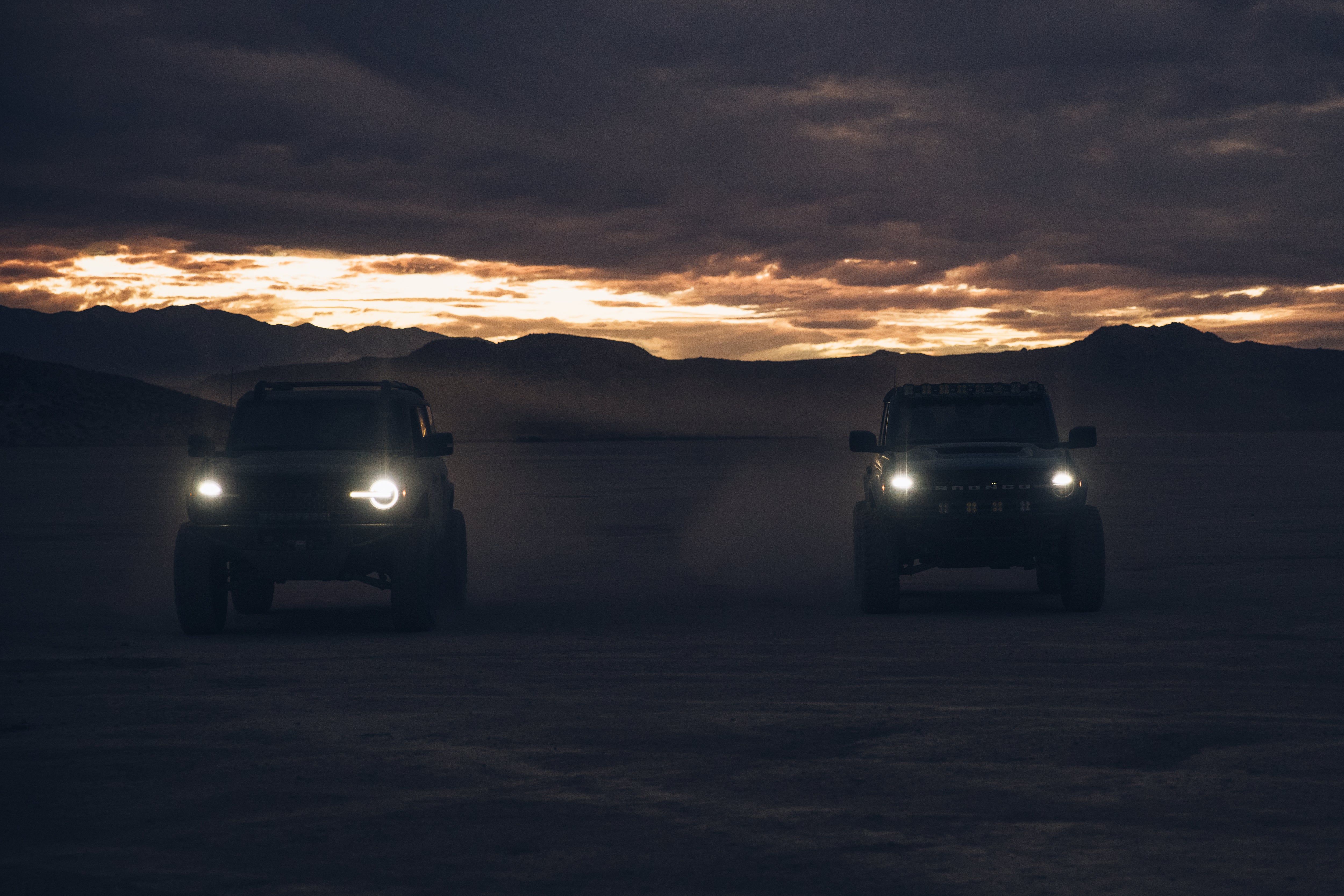 Two 2021 Ford trucks with ADV fiberglass parts driving on a sandy terrain at sunset, showcasing offroad capabilities.