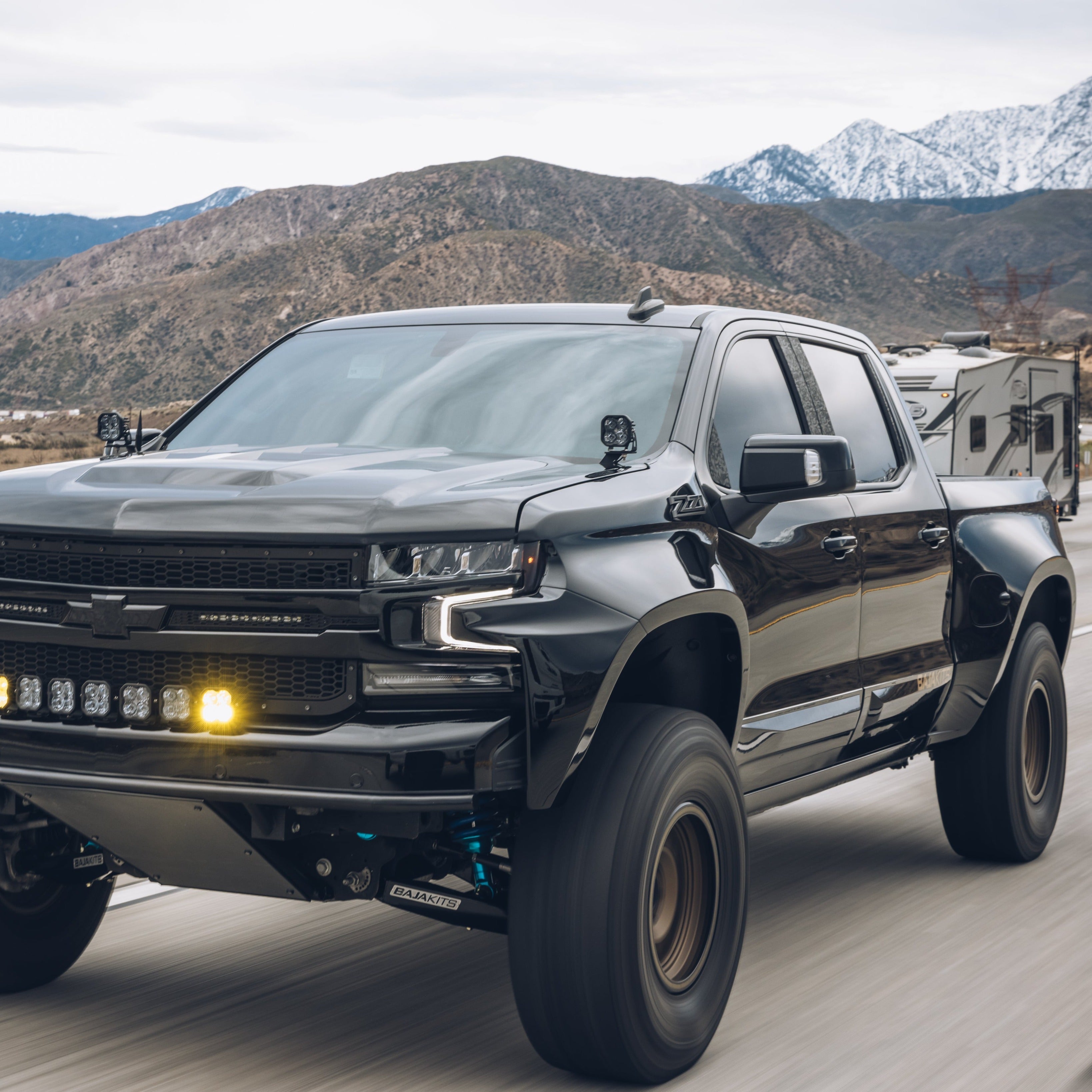 2019-2025 Chevrolet Silverado with custom bedsides driving on a scenic road, showcasing offroad capabilities and rugged design.