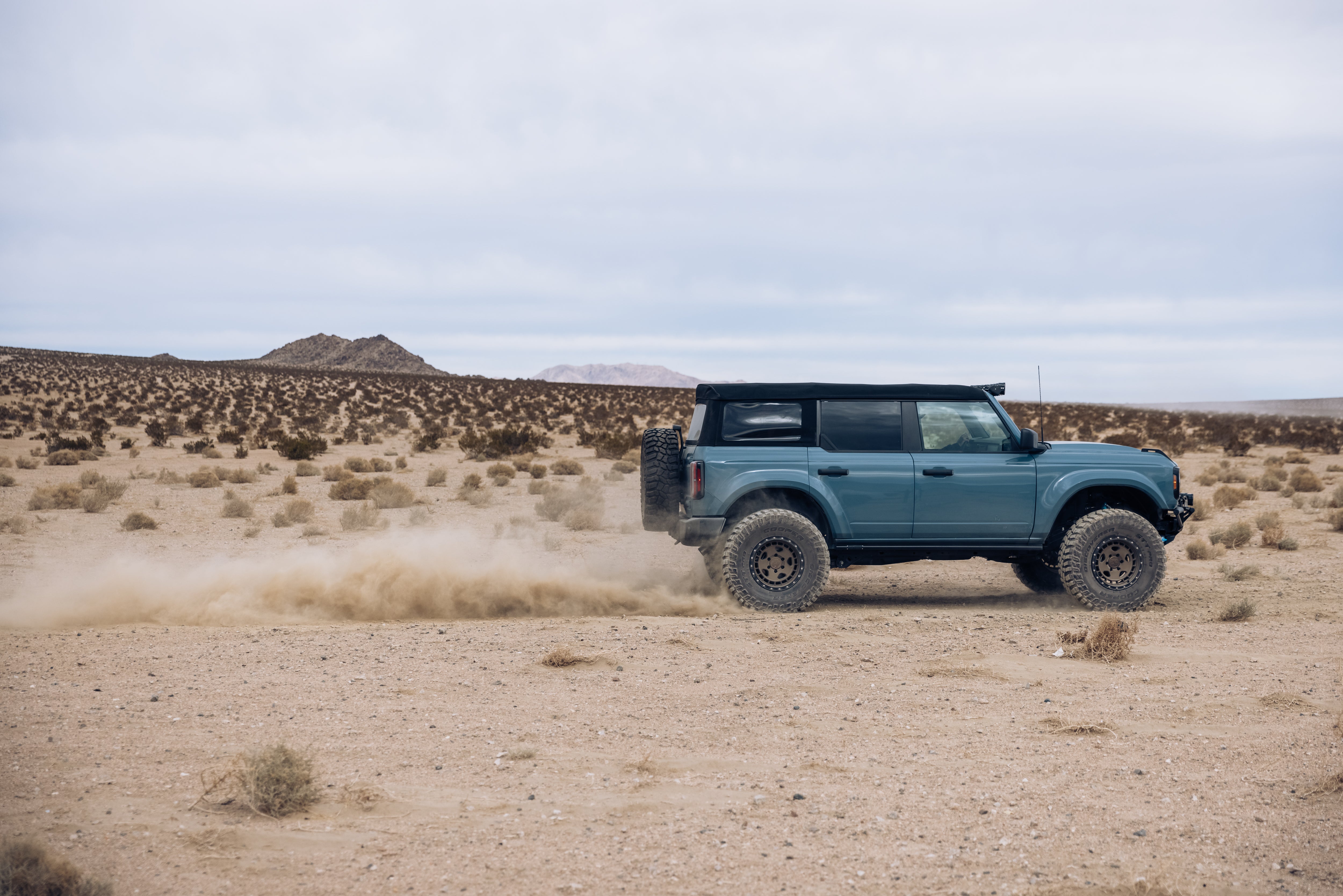 ADV Fiberglass 2021 Ford vehicle driving through a desert landscape, kicking up dust with rugged terrain in the background.