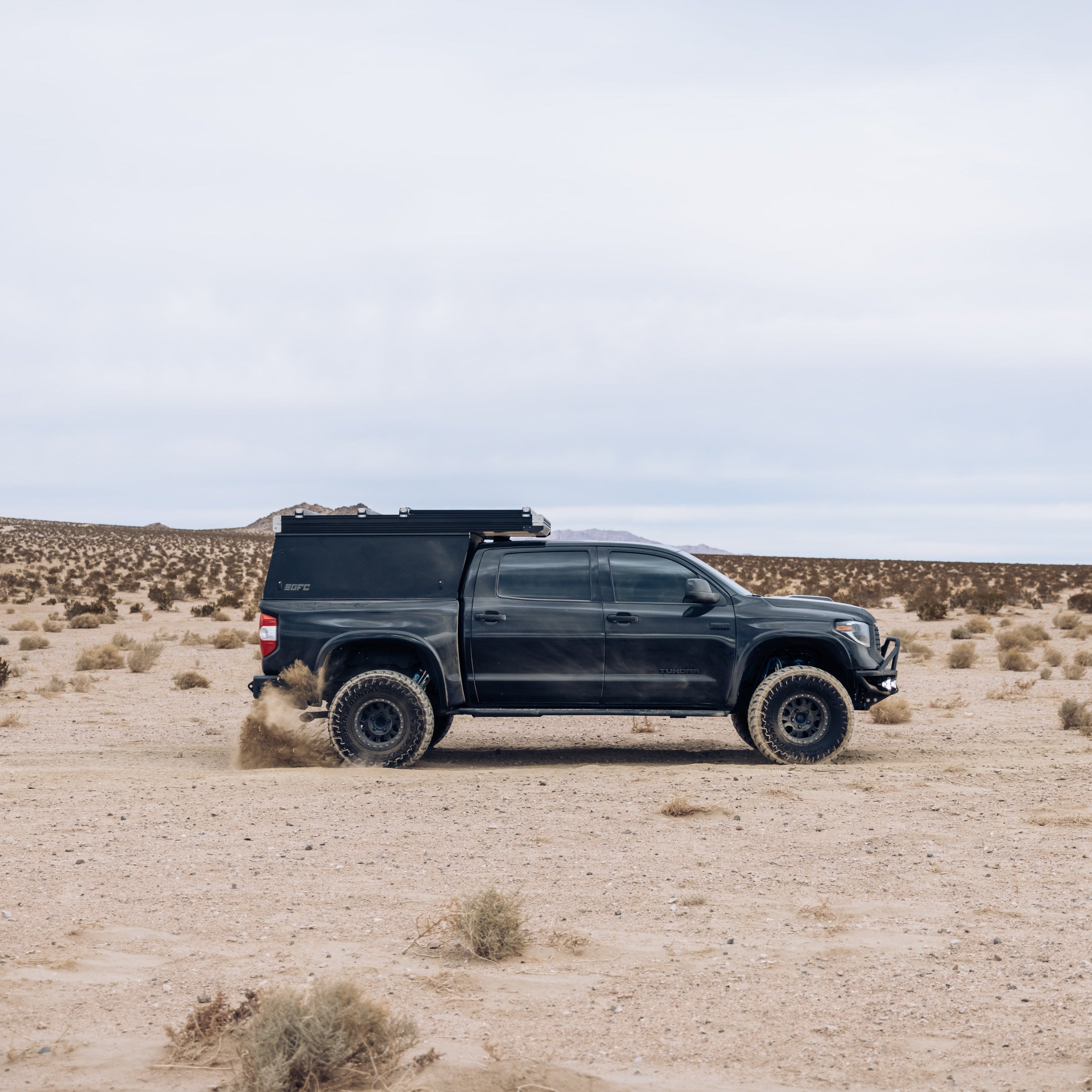 Black 2014-2021 Toyota Tundra with aftermarket fenders driving through a desert landscape, showcasing offroad capability.