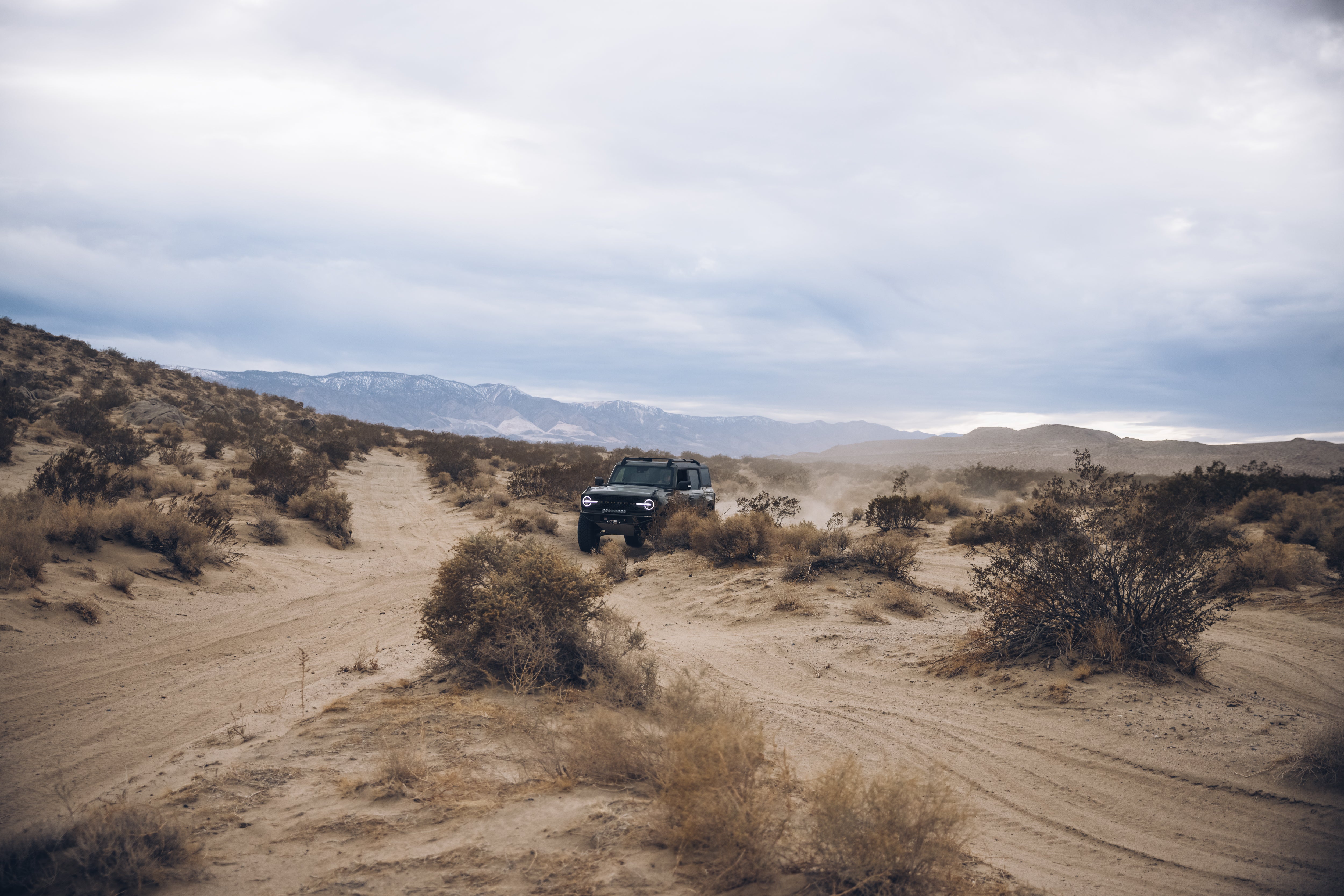 2021 Outer Banks BAJA FORGED navigating a rugged desert landscape with dust clouds and distant mountains.