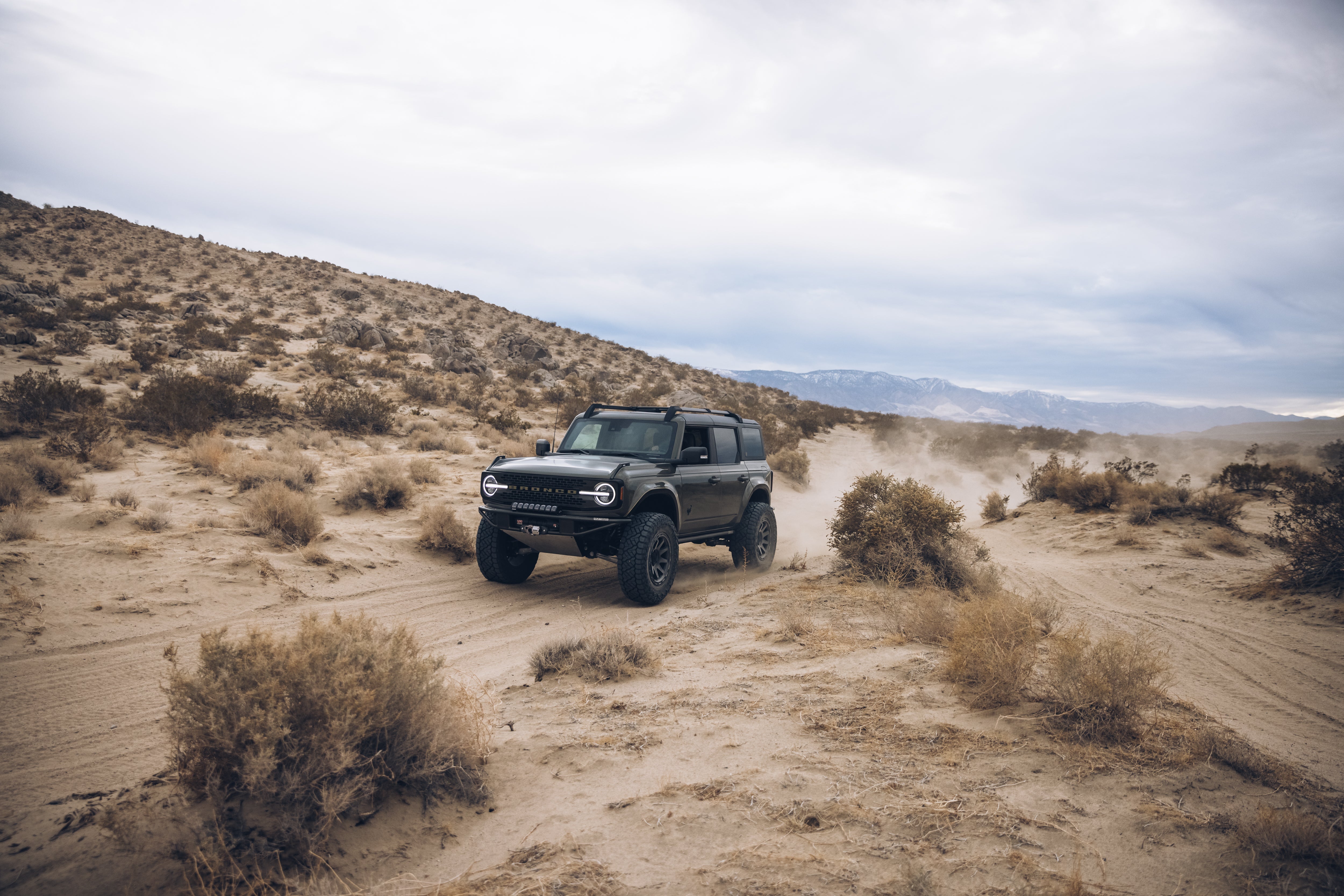 2021 Outer Banks BAJA FORGED off-road vehicle navigating a sandy desert landscape with rugged terrain and sparse vegetation.