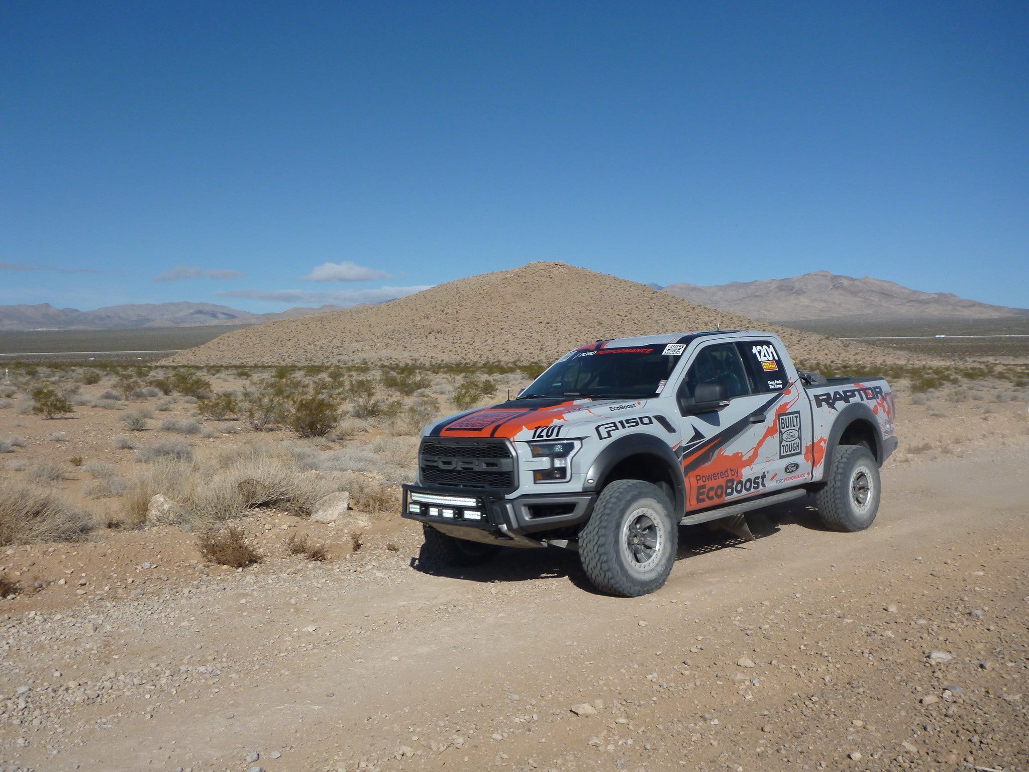 Ford Raptor race truck equipped with a front bumper light bar mount kit, driving on a desert road.
