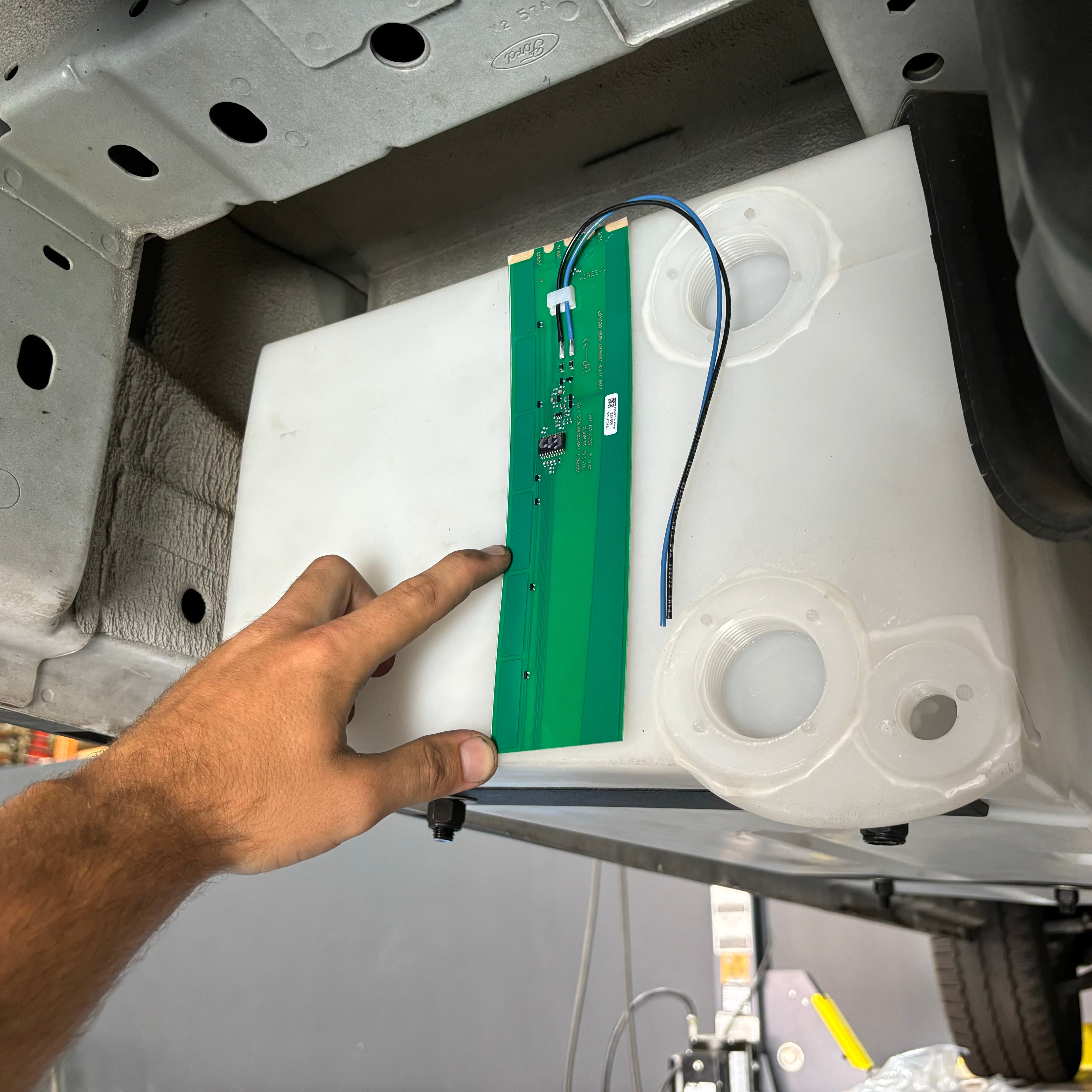 22-gallon undercarriage fresh/grey water tank for 2015-2025 Ford Transit, showing installation with wiring and fittings.