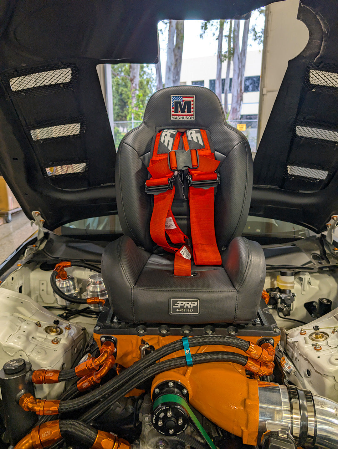 High-performance B.O.O.S.T.E.R. S.E.A.T. installed in a vehicle engine bay, showcasing racing harness and sleek design.