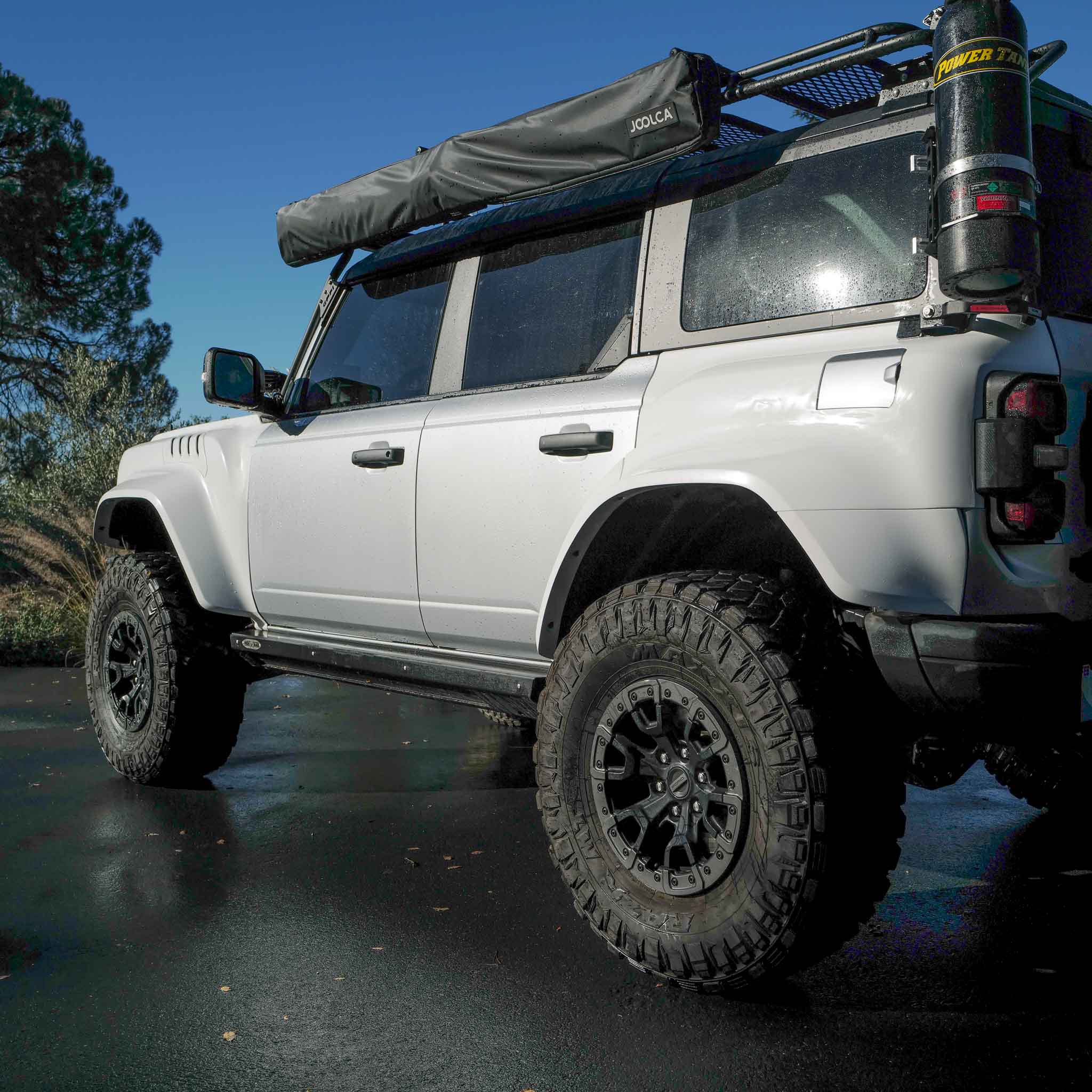 2022-2025 Ford Bronco Raptor with rear quarter kit, showcasing rugged tires and off-road accessories in a natural setting.
