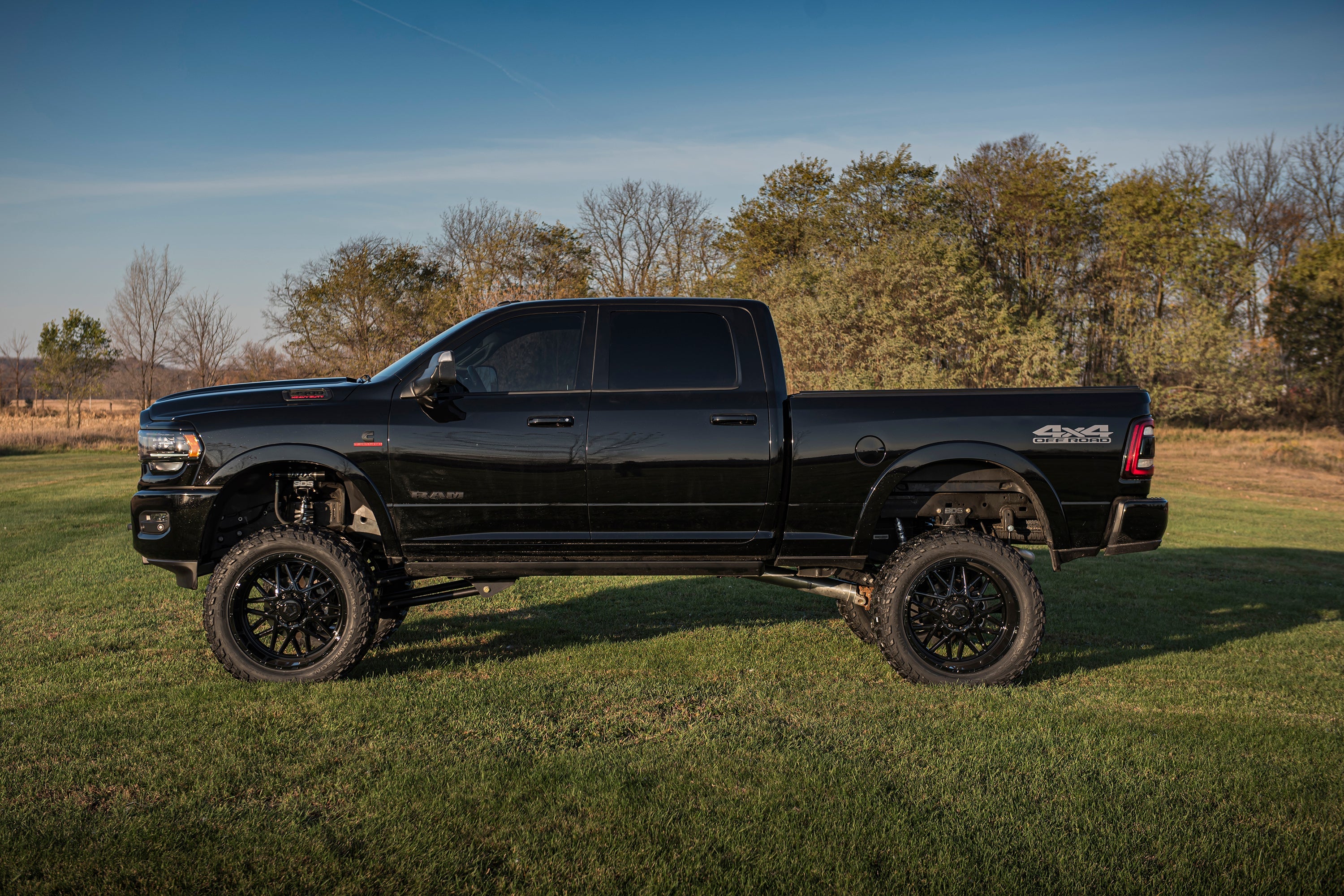 Black Ram 2500 truck with an 8-inch lift kit and 4-link suspension, parked on grass in a scenic outdoor setting.