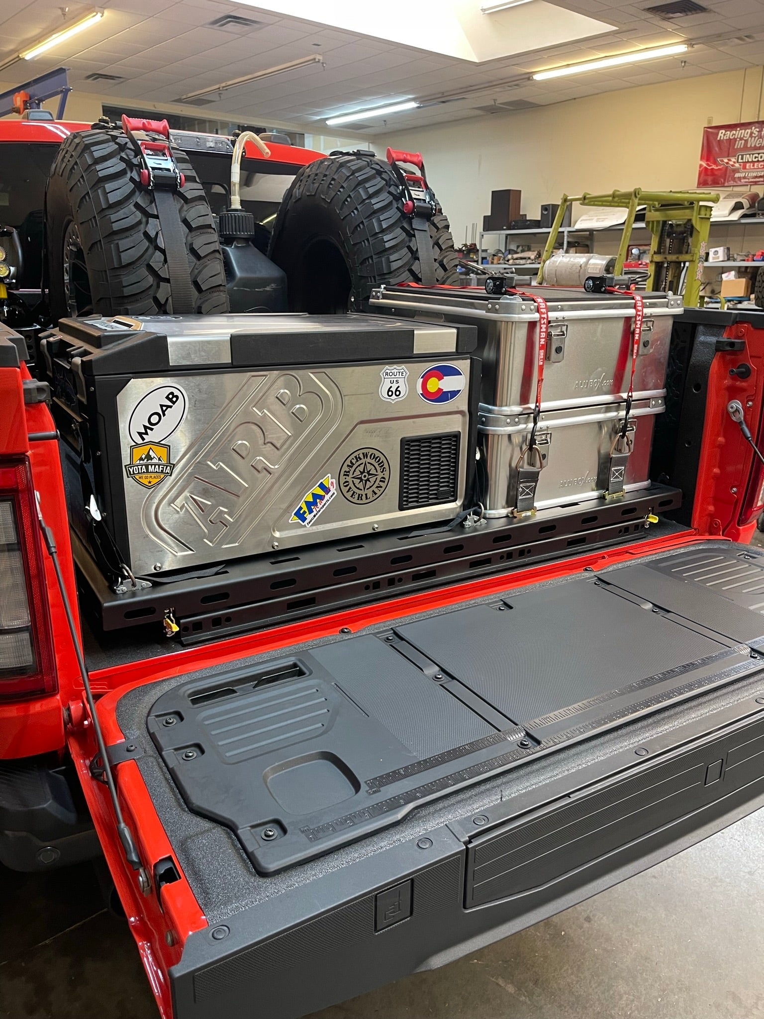 Raptor rear bed organizer with cargo slide tray, featuring a mounted cooler and gear, designed for efficient truck storage.