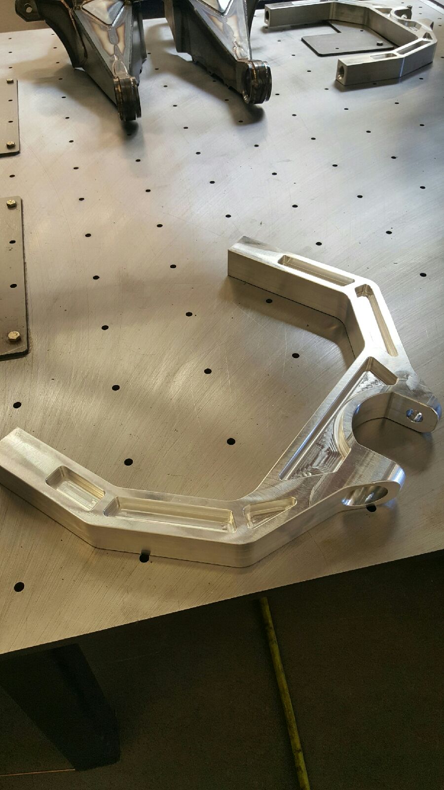 2017 Up Raptor Long Travel Front Suspension Kit component showcasing a polished aluminum control arm on a workbench.
