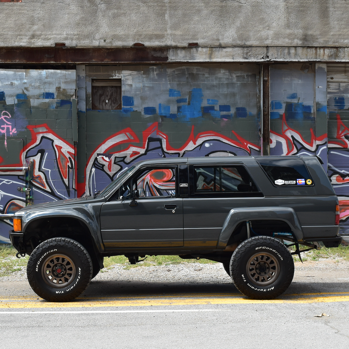 1984-1988 Toyota Pickup fenders displayed on a lifted truck against a colorful graffiti backdrop.