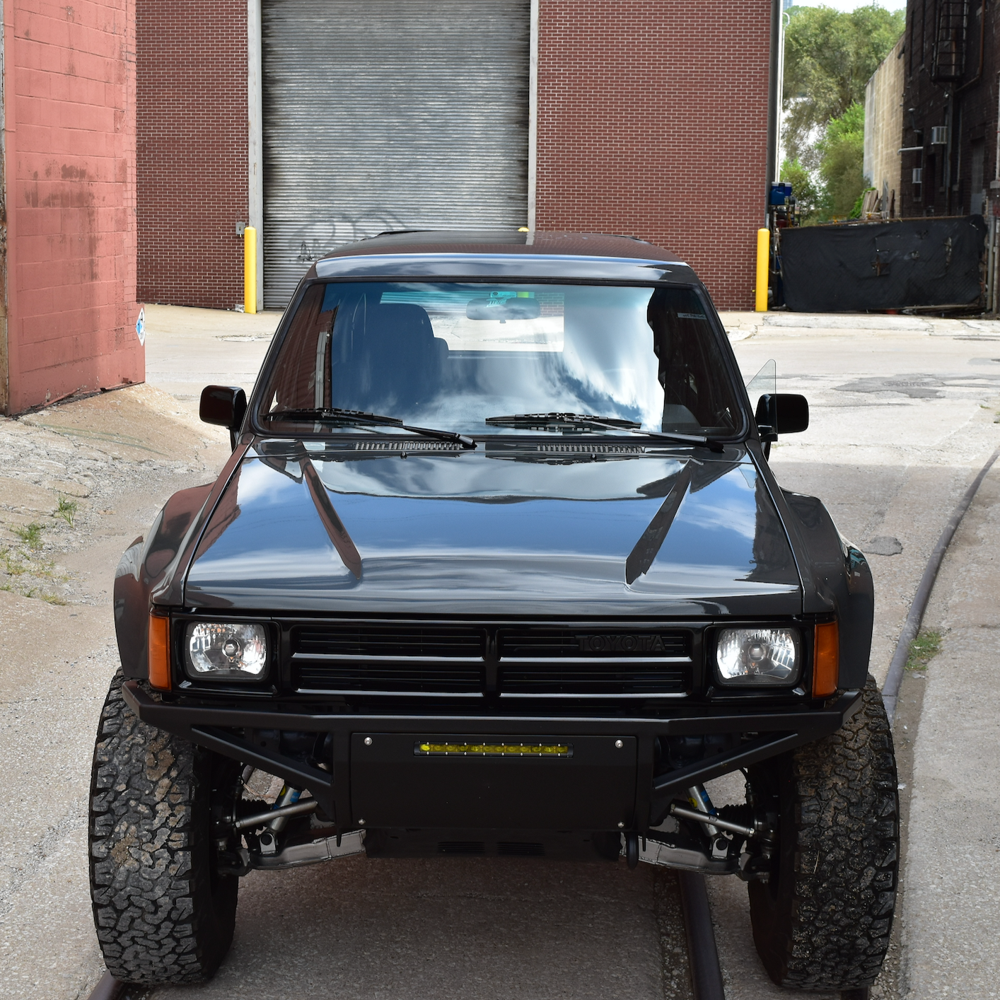 Front view of a black 1984-1988 Toyota Pickup showcasing custom fenders, highlighting its off-road capabilities.