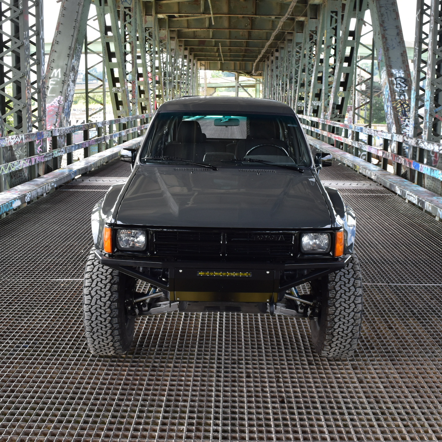 Black 1984-1988 Toyota Pickup on a metal bridge, showcasing custom fenders and offroad tires.