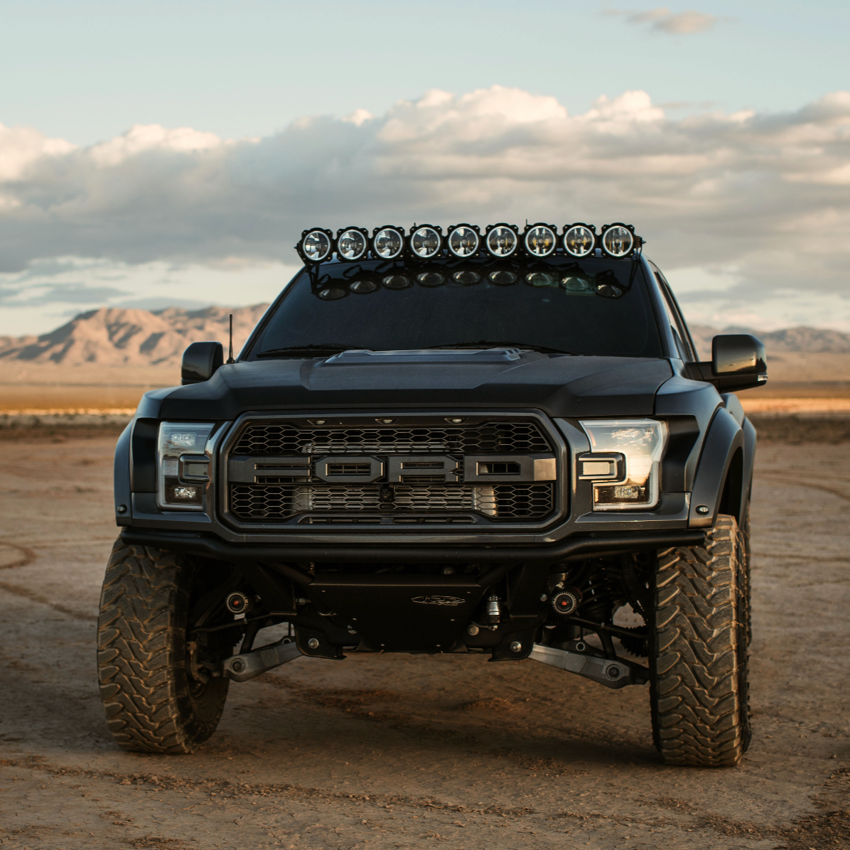 2017-2020 Ford Raptor with aftermarket fenders and roof-mounted lights, set against a desert landscape.