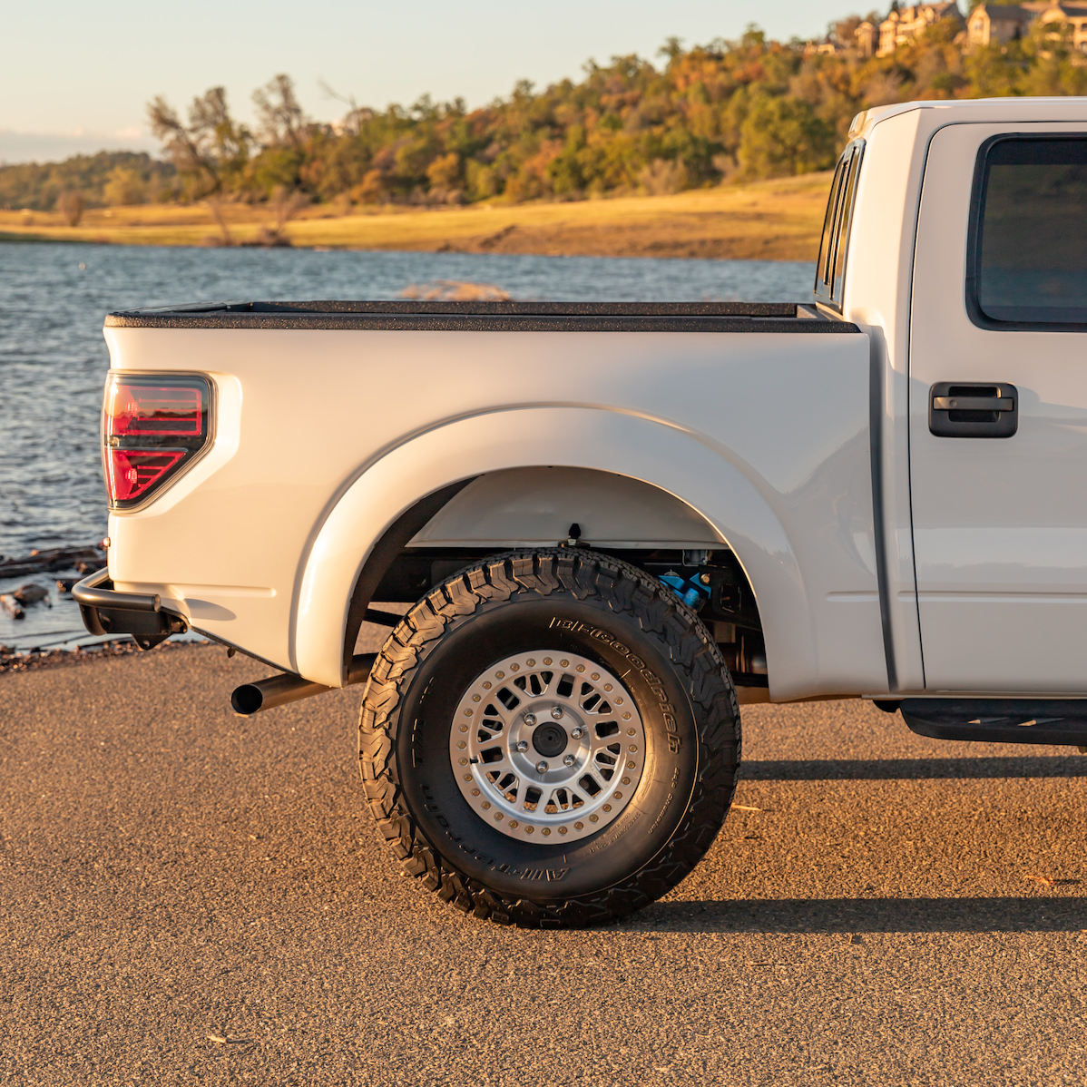 2010-2016 Ford Raptor bedsides showcasing a custom fit on a truck with offroad tires by a scenic lake.